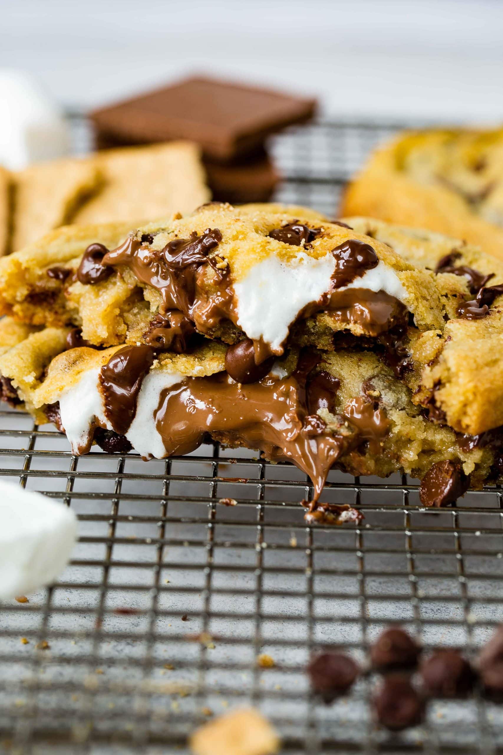 A s'mores stuffed chocolate chip cookie. The cookie is broken in half showing the chocolate, marshmallow and graham cracker inside of the chocolate chip cookie.