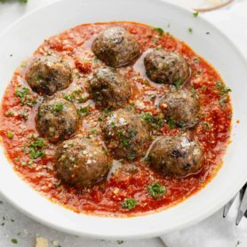 A bowl of meatballs in a tomato based sauce. The dish is sprinkled with chopped parsley.