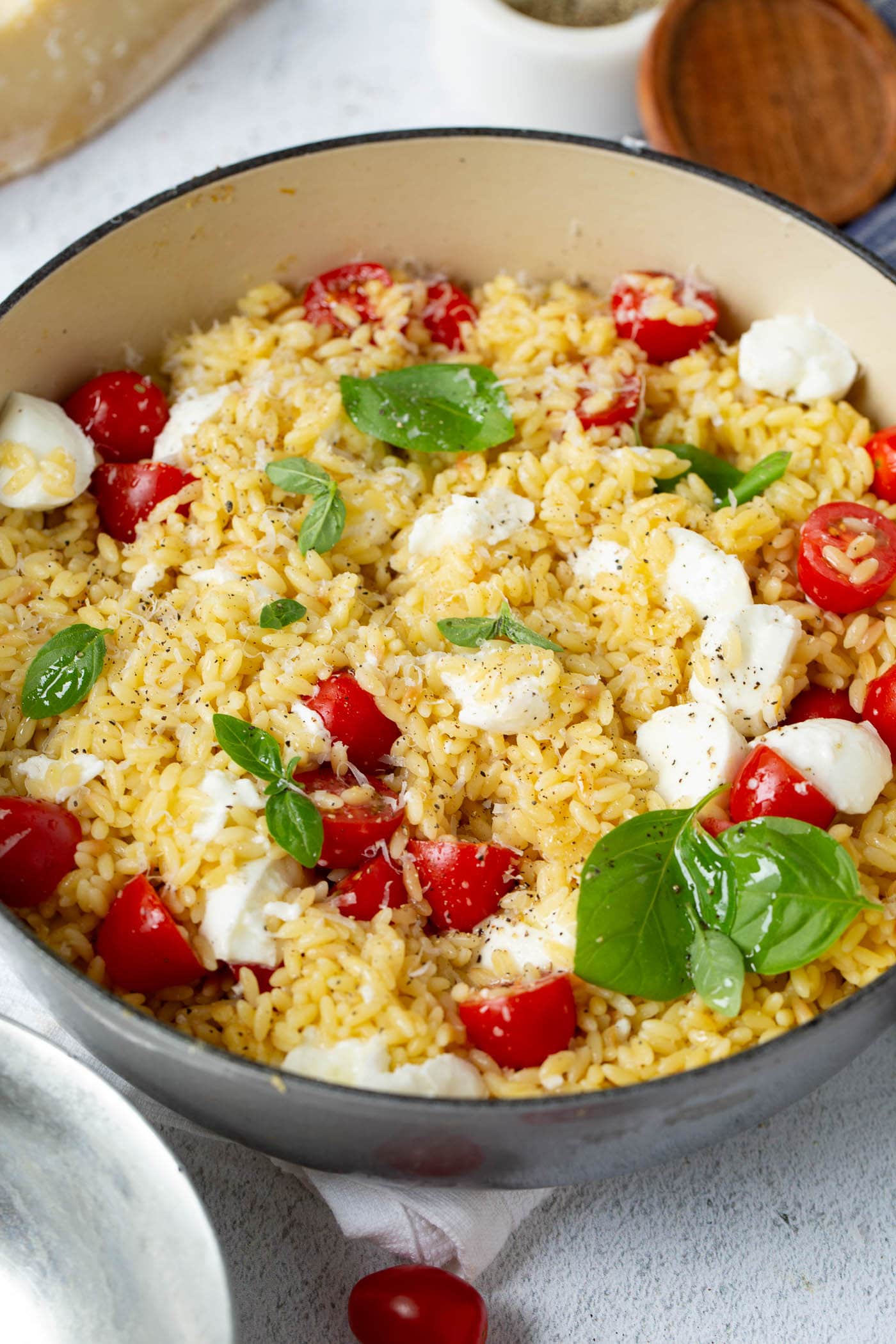 A close-up of caprese orzo salad. It has red tomatoes, fresh green basil, and chunks of mozzarella cheese.