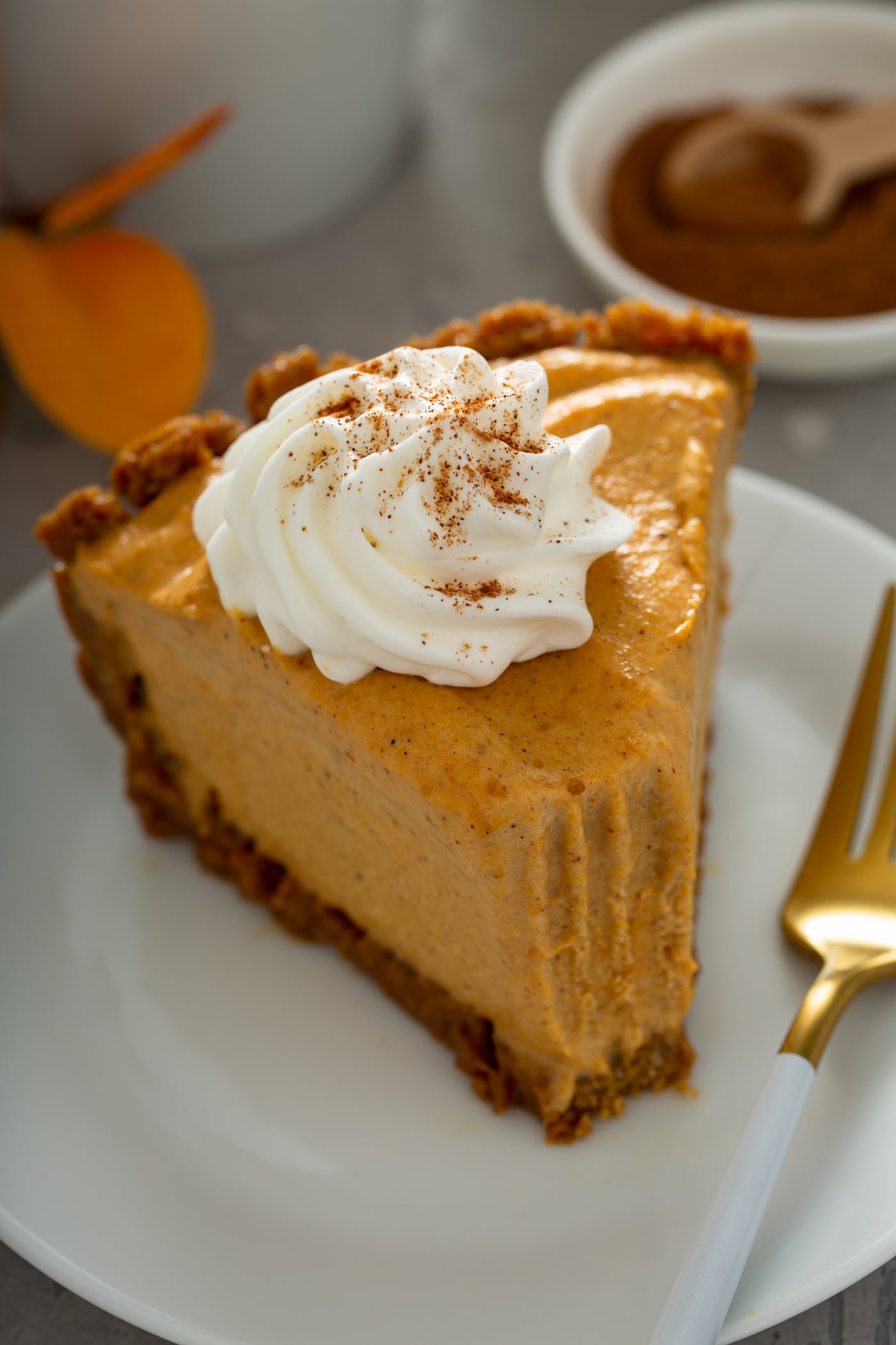 A slice of pumpkin ice cream pie with a fork next to it. A bite has been taken in the pie and it is topped with a dollop of whipped cream sprinkled with cinnamon.