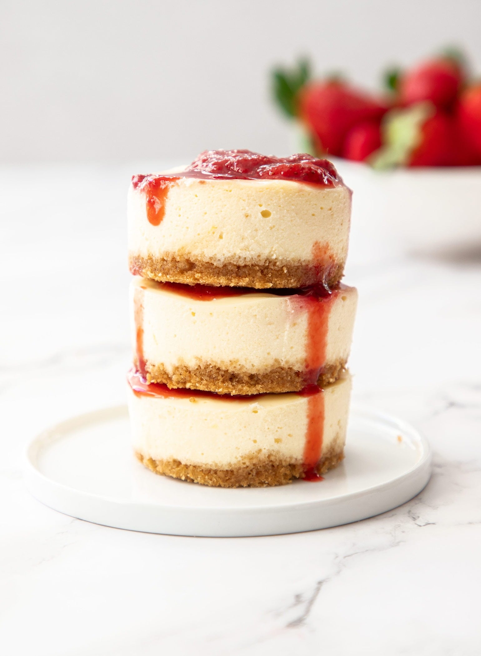 3 mini strawberry cheesecakes stacked on top of each other on a small white plate