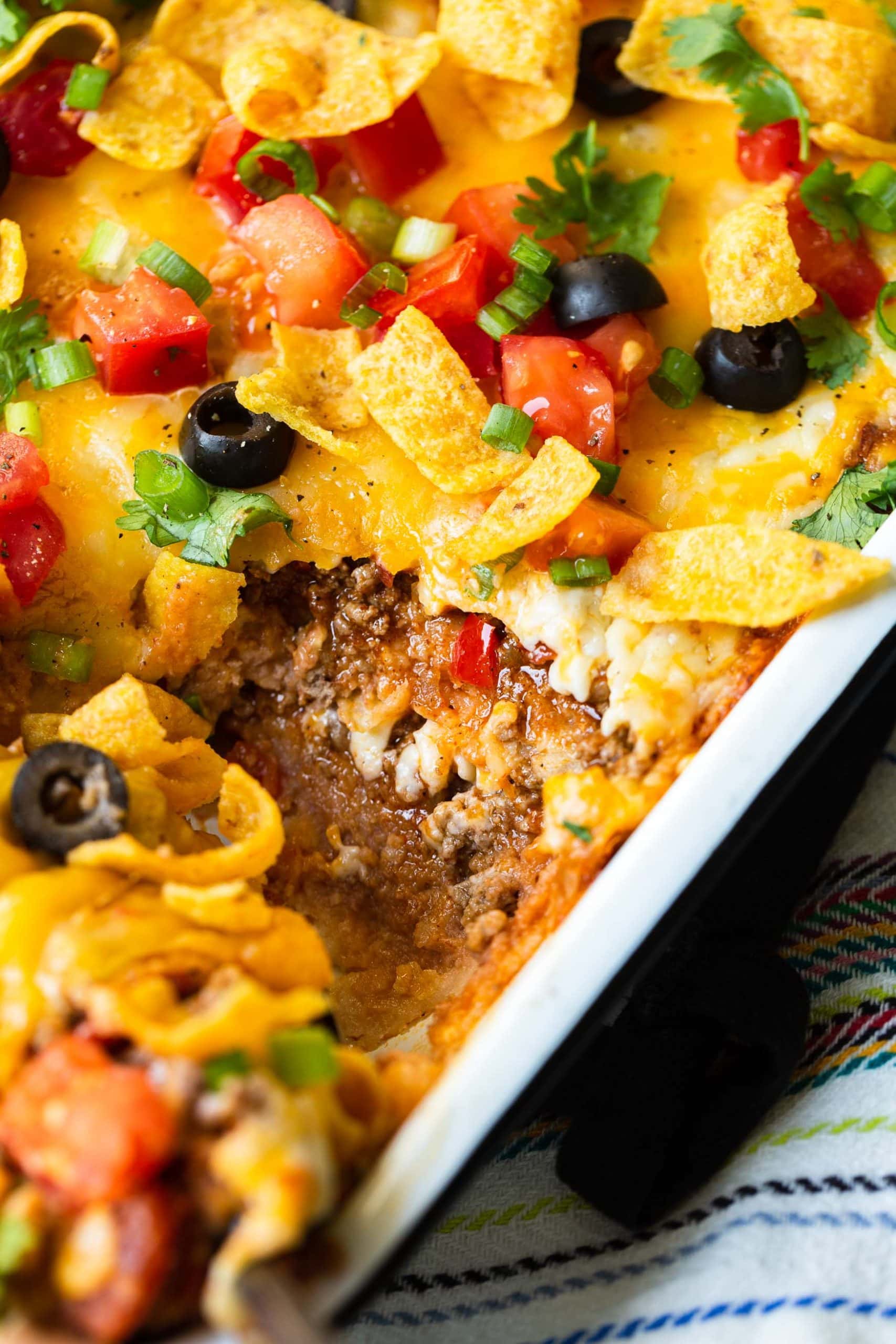 a close up photo of a taco casserole in the dish and one piece is missing so you can see the layer inside.