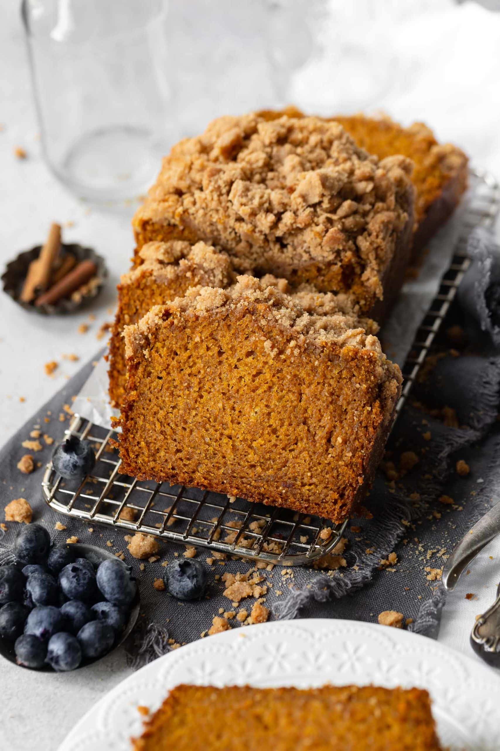 a photo of a loaf of pumpkin bread with a streusel topping cut into slices and fanned out on a wire cooling rack.