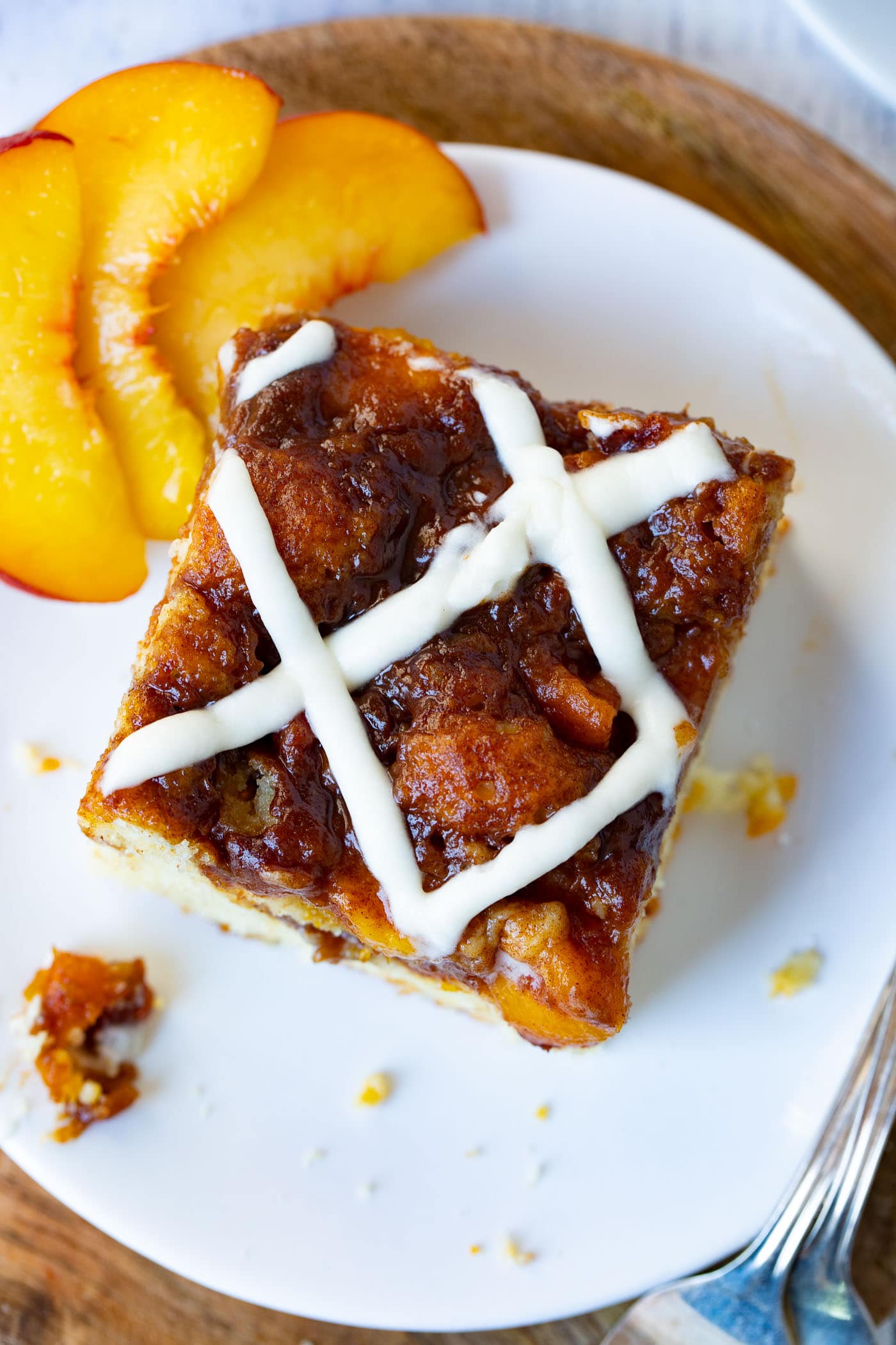 a photo of a single piece of peacch coffee cake topped with a sweet glaze sitting on white plate with three peach slices sitting next to it.