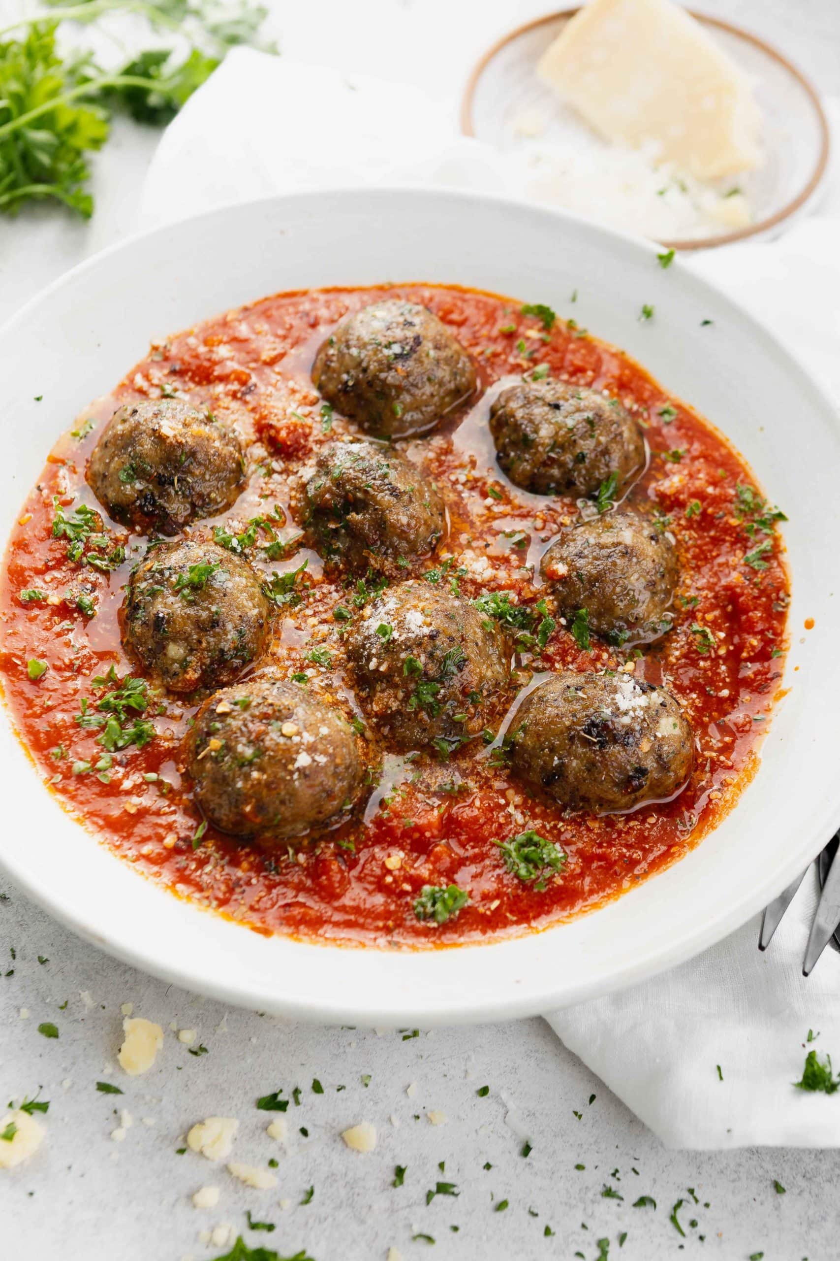 A bowl of meatballs in a tomato based sauce. The dish is sprinkled with chopped parsley.