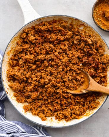 Chorizo pork in a white pan with a wooden spoon