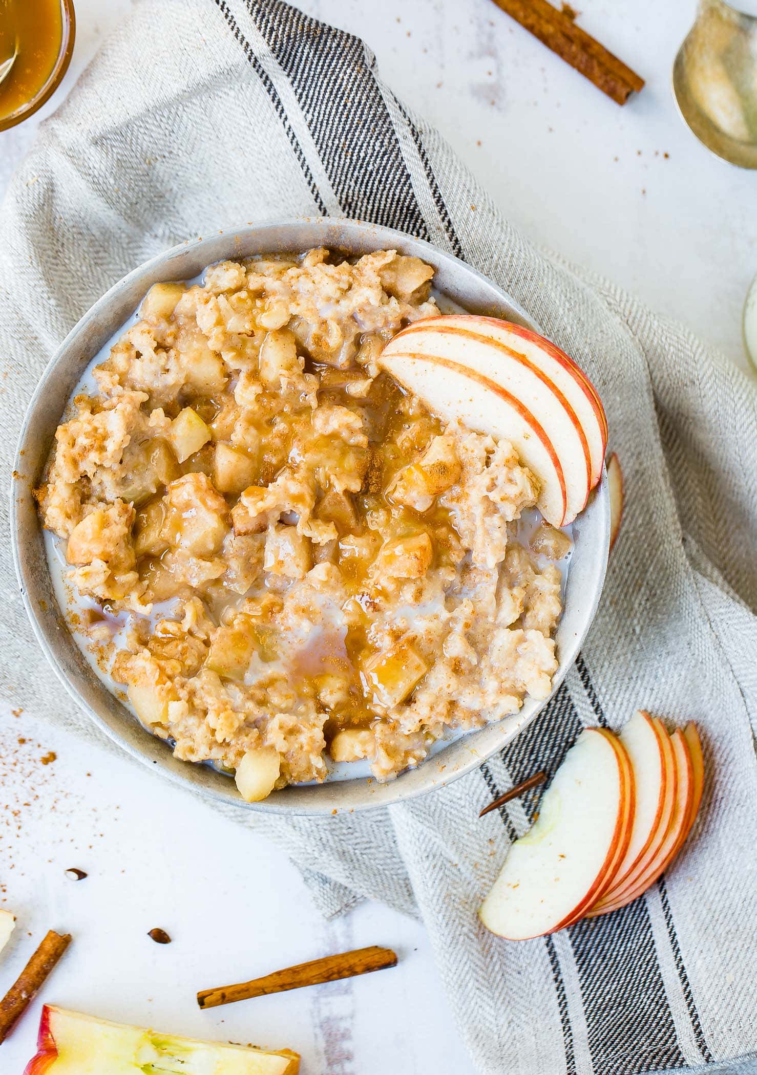 A photo of a bowl of apple pie slow cooker oatmeal with caramel and thinly sliced apples on top with milk added