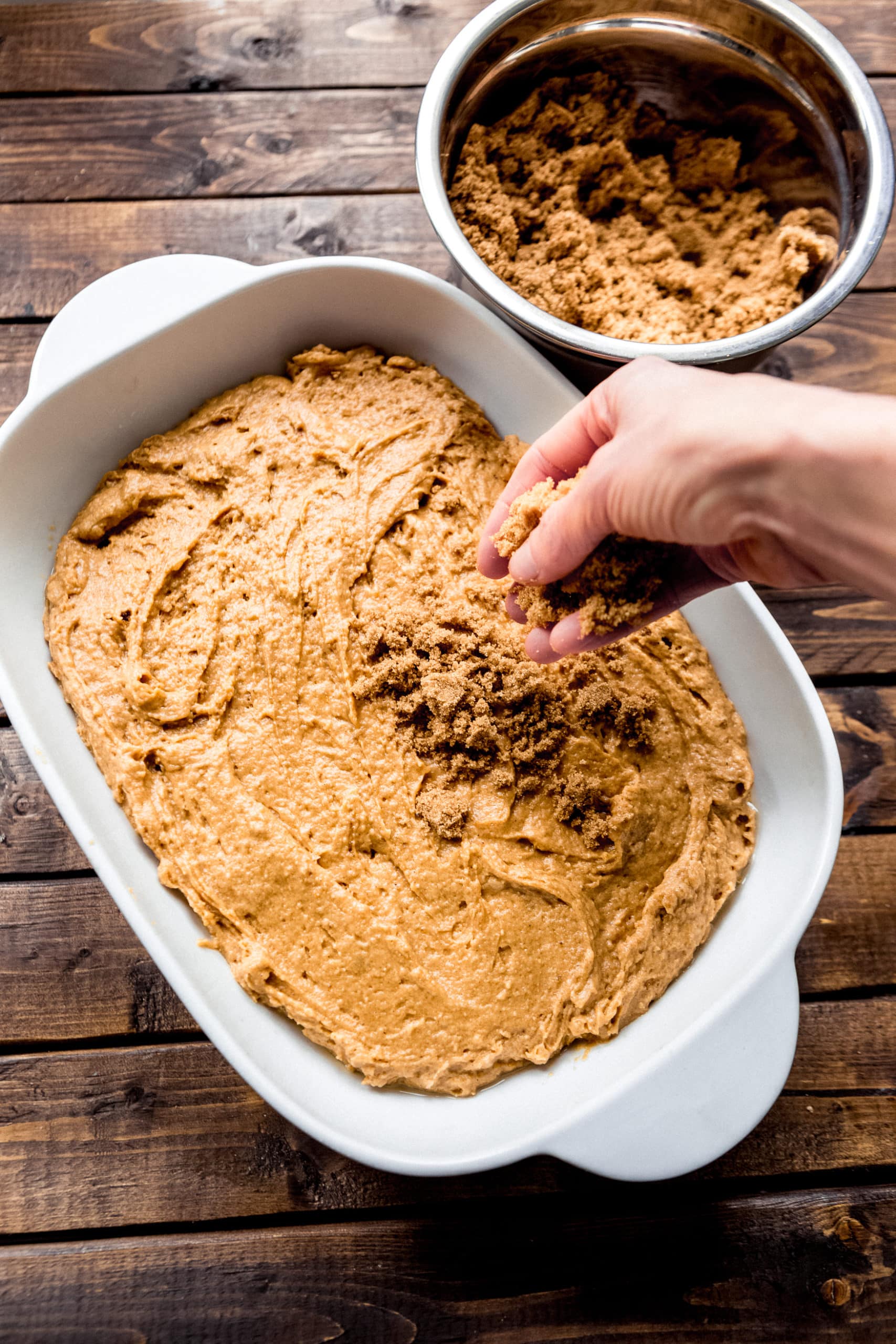 a photo of a someone sprinkling a brown sugar topping on top of pumpkin lava cake batter in a white rectangular baking dish.