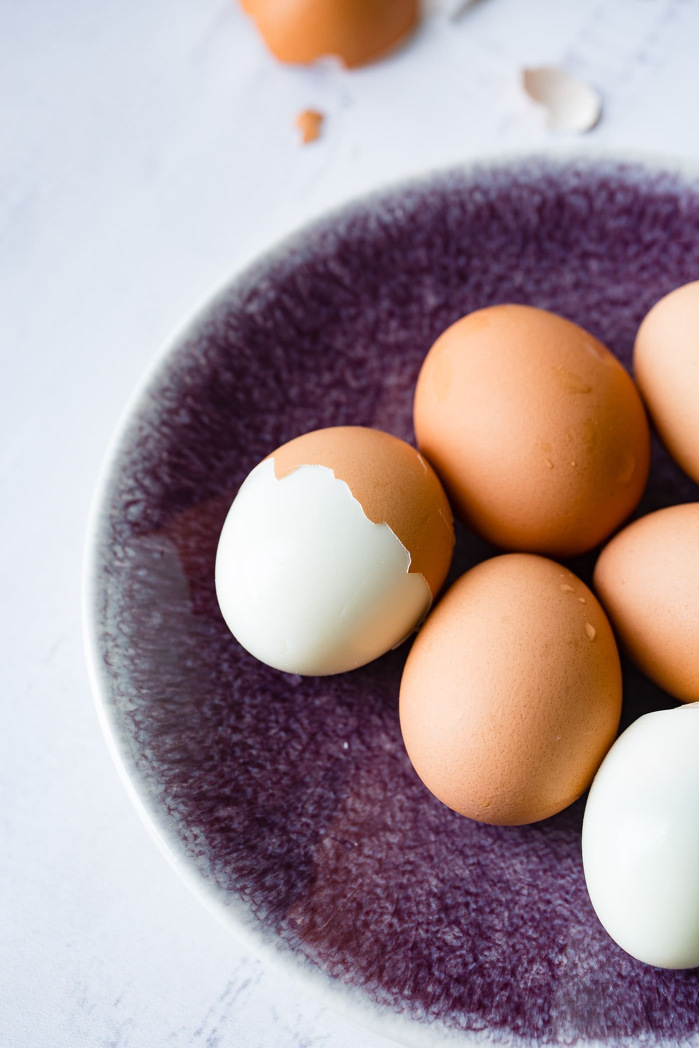 A plate with 6 brown hard boiled eggs. On egg is peeled and another egg is partially peeled.