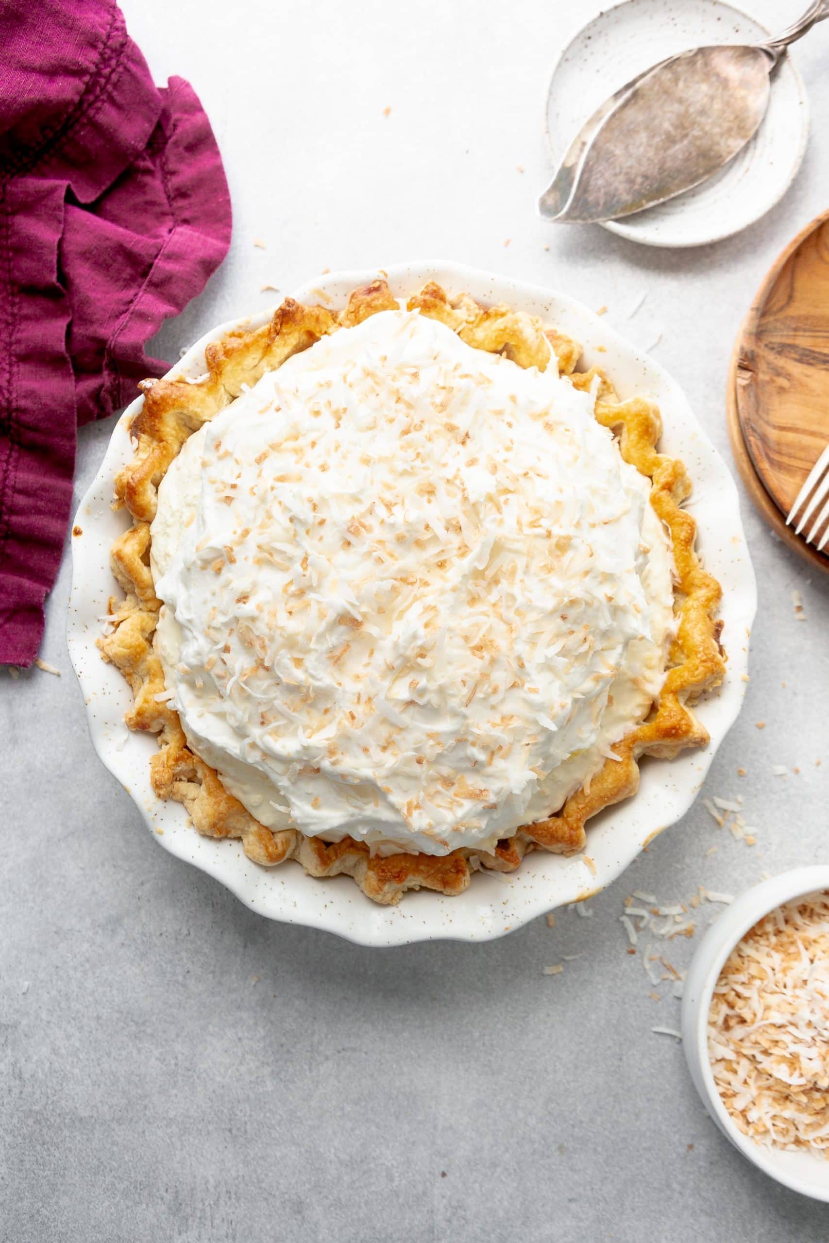 a photo of a whole coconut cream pie in a white pie dish and homemde crust topped with toasted shredded coconut.