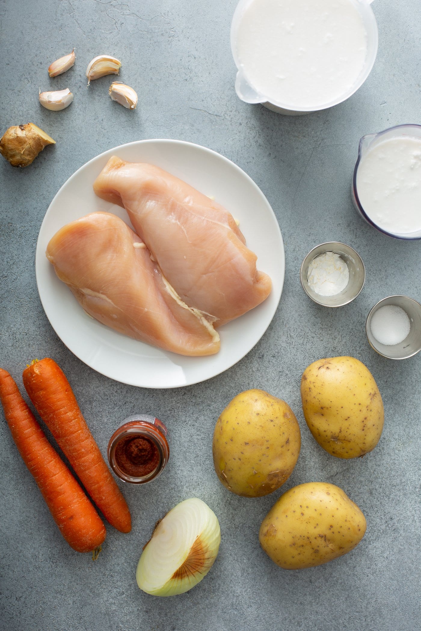 Ingredients for chicken curry. There are three peeled potatoes, two carrots, two chicken breasts, and curry paste, garlic, onion, cream, and salt.