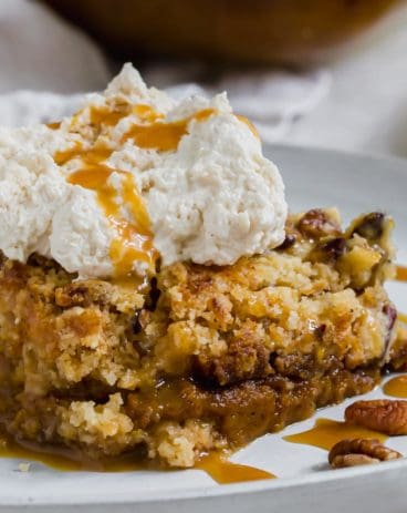 Slice of pumpkin dump cake with whipped cream and caramel sauce drizzled on top.