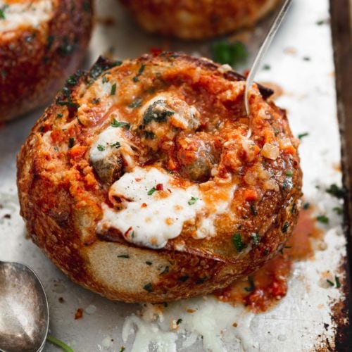 A bread bowl filled with parmesan meatball soup. The bread bowl and soup have been baked to a perfect toasty brown and the cheese on top is gooey melted perfection.