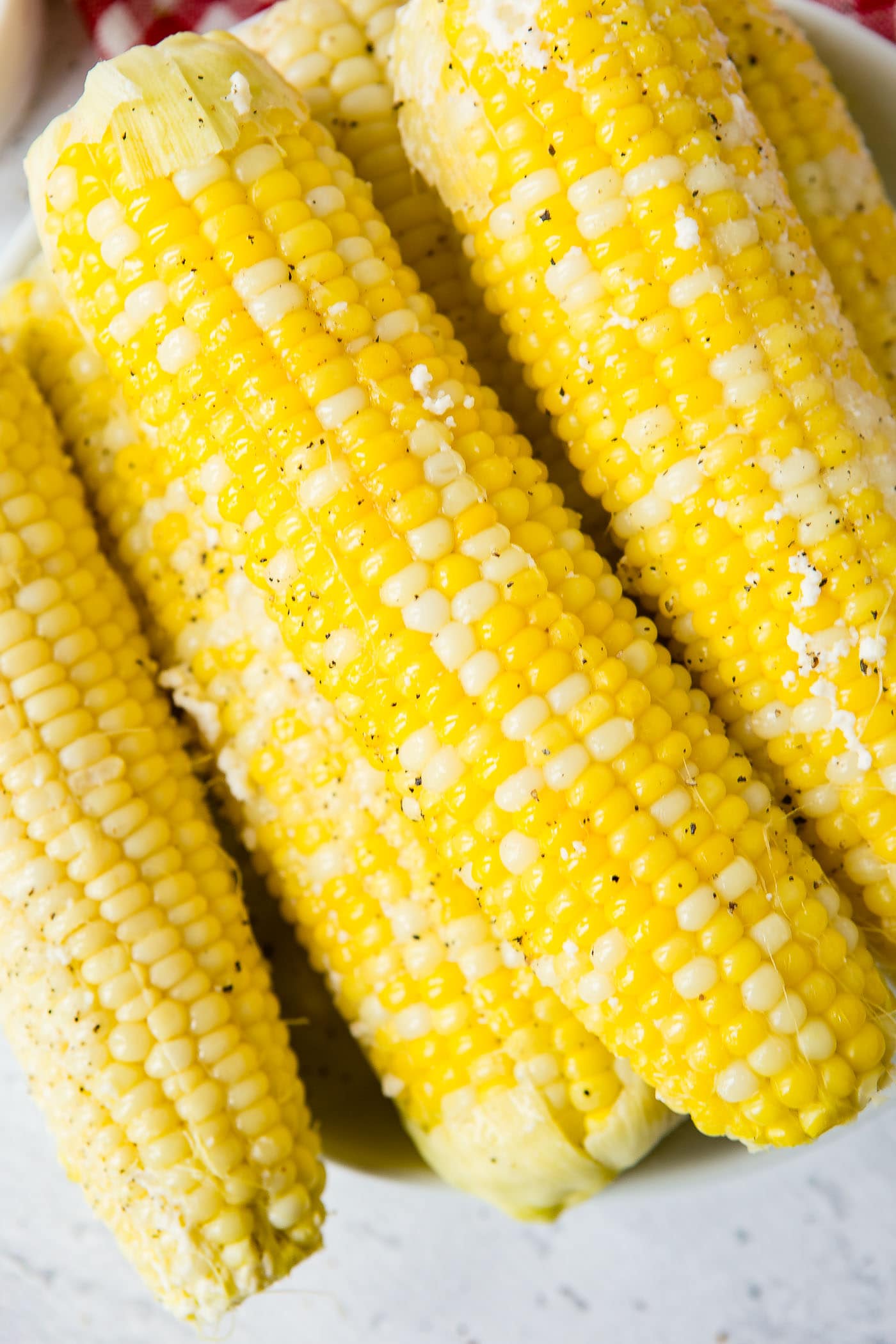 A close-up of four ears of cooked corn on the cob sprinkled with ground pepper.