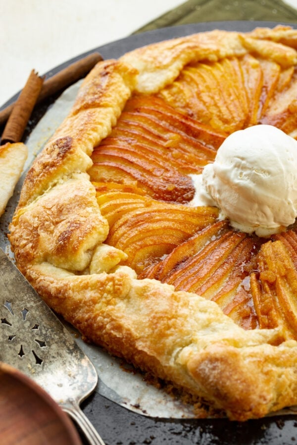 a photo of a sugar pear galette with golden rustic crust and a scoop of vanilla ice cream on top.
