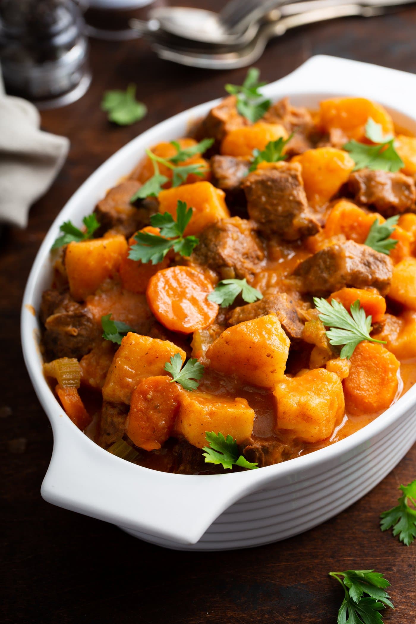A serving bowl of instant pot beef stew. There are chunks of carrots, beef, and potatoes in a rich brown sauce. An instant pot and linen napkin are in the background.