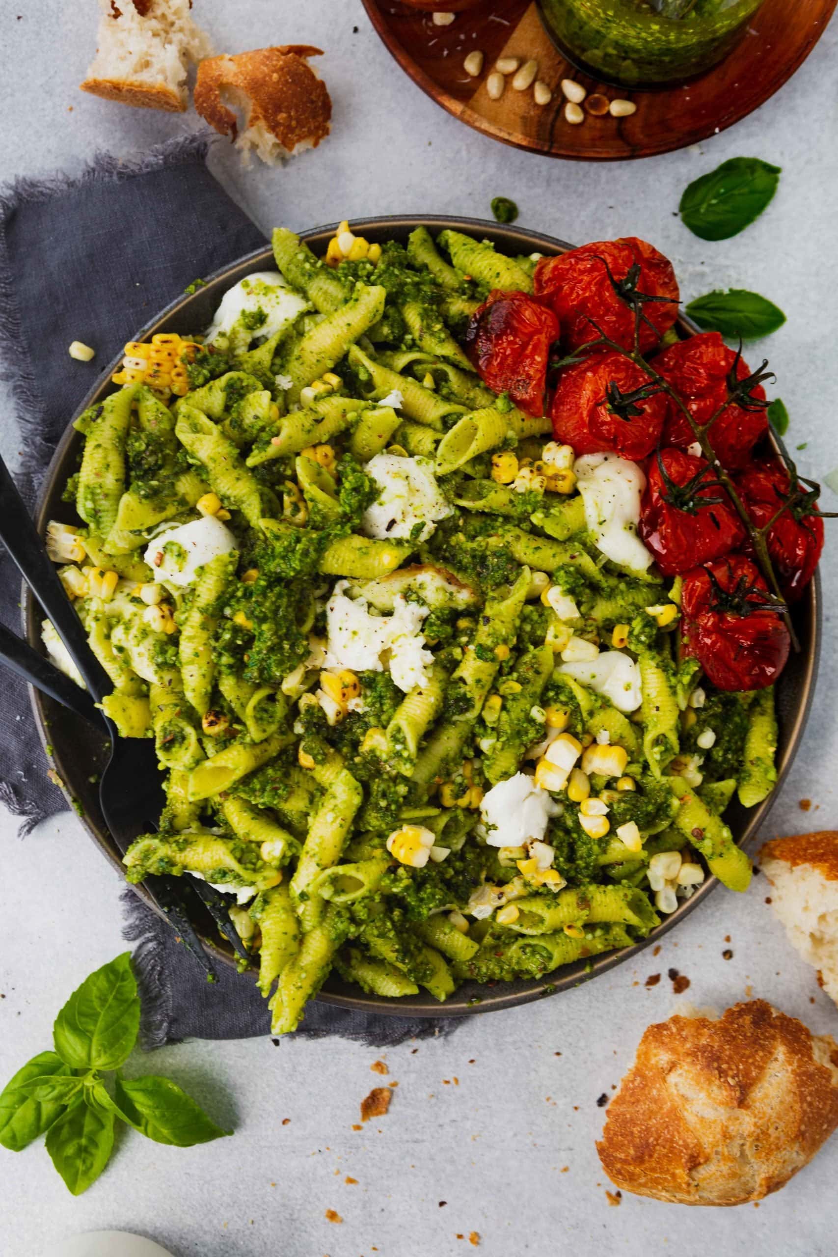 a photo of a bowl full of pesto pasta topped with grilled corn, mozzarella balls and roasted tomatoes.