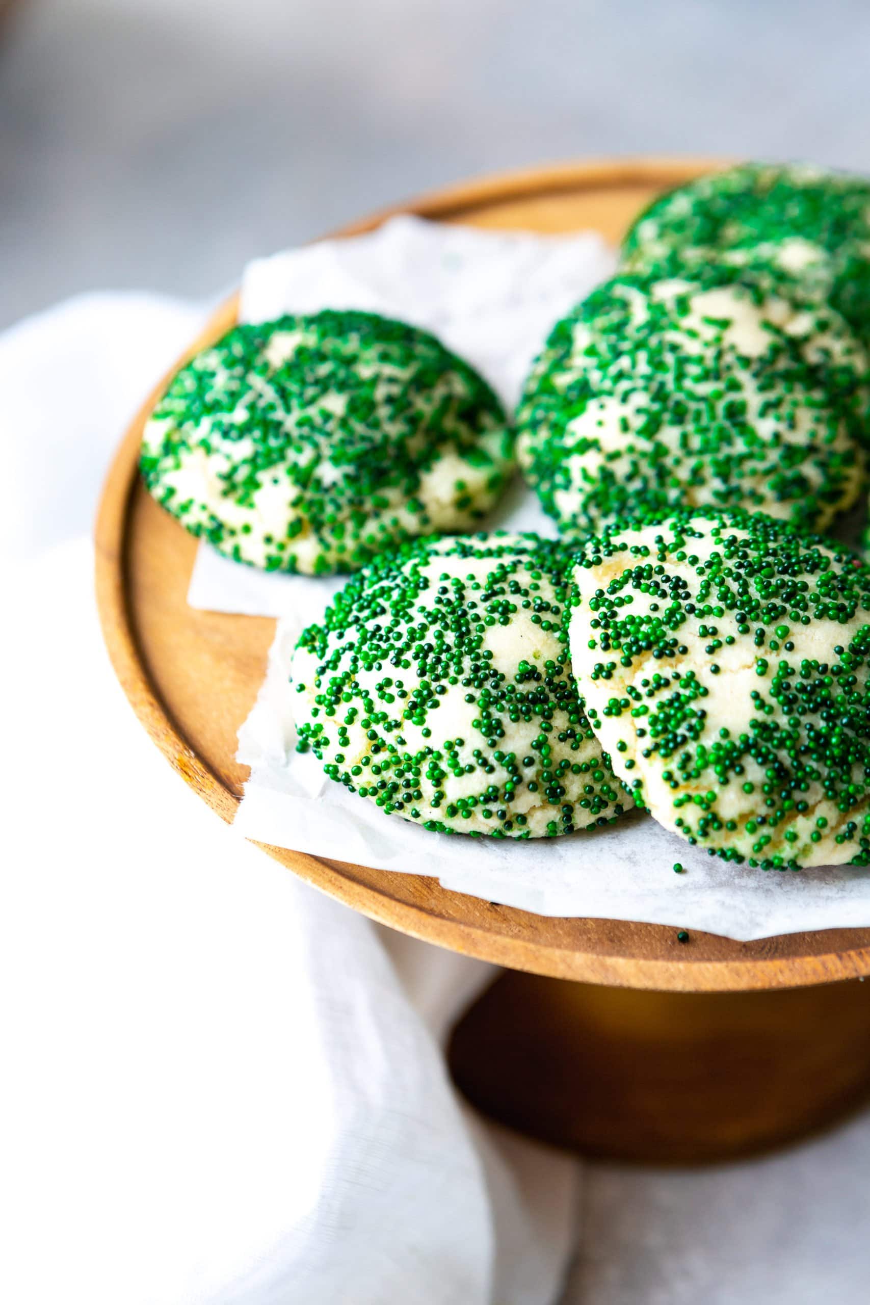 a photo of several sugar cookie covered in dark green sprinkles sitting on a wooden serving tray.