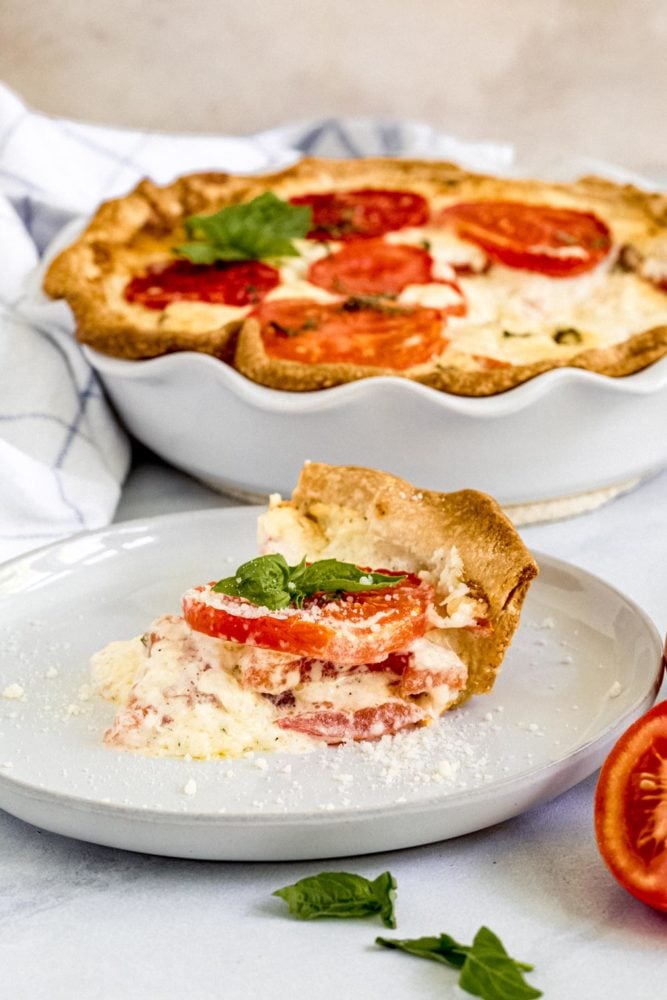 Alabama Tomato Pie slice on white plate with pie dish behind it.