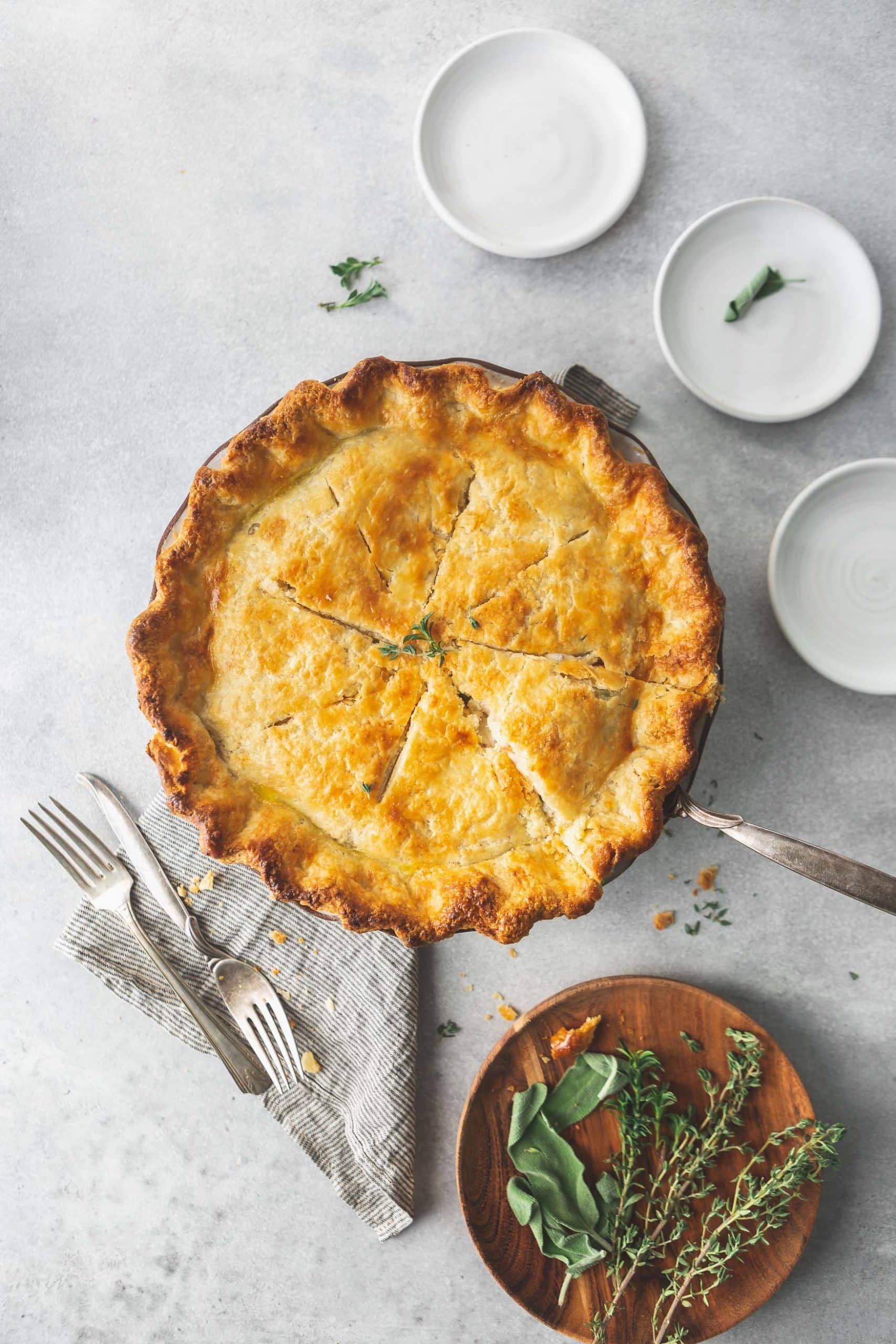A baked turkey pot pie. The crust is golden brown and there are forks next to the pie and small containers of ingredients sitting next to the pie.