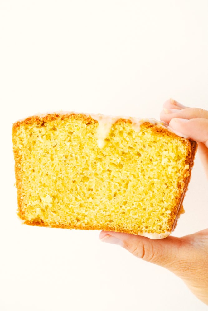 Slice of glazed lemon bread in a photo being held up by a hand. 