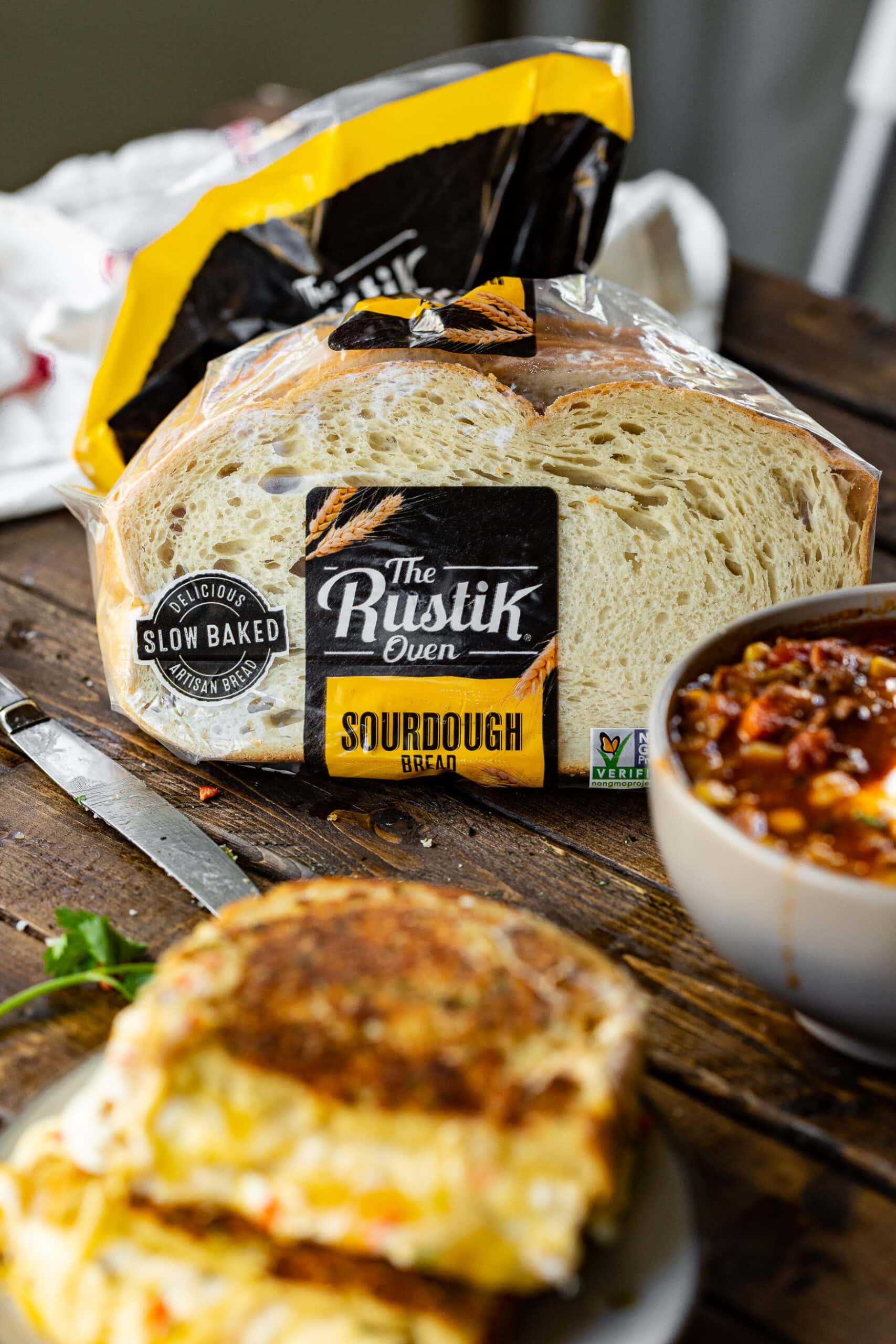 a photo of a grilled Mexican cheese sandwich sitting on a small plate with a bowl of taco stew and a bag of sourdough bread.