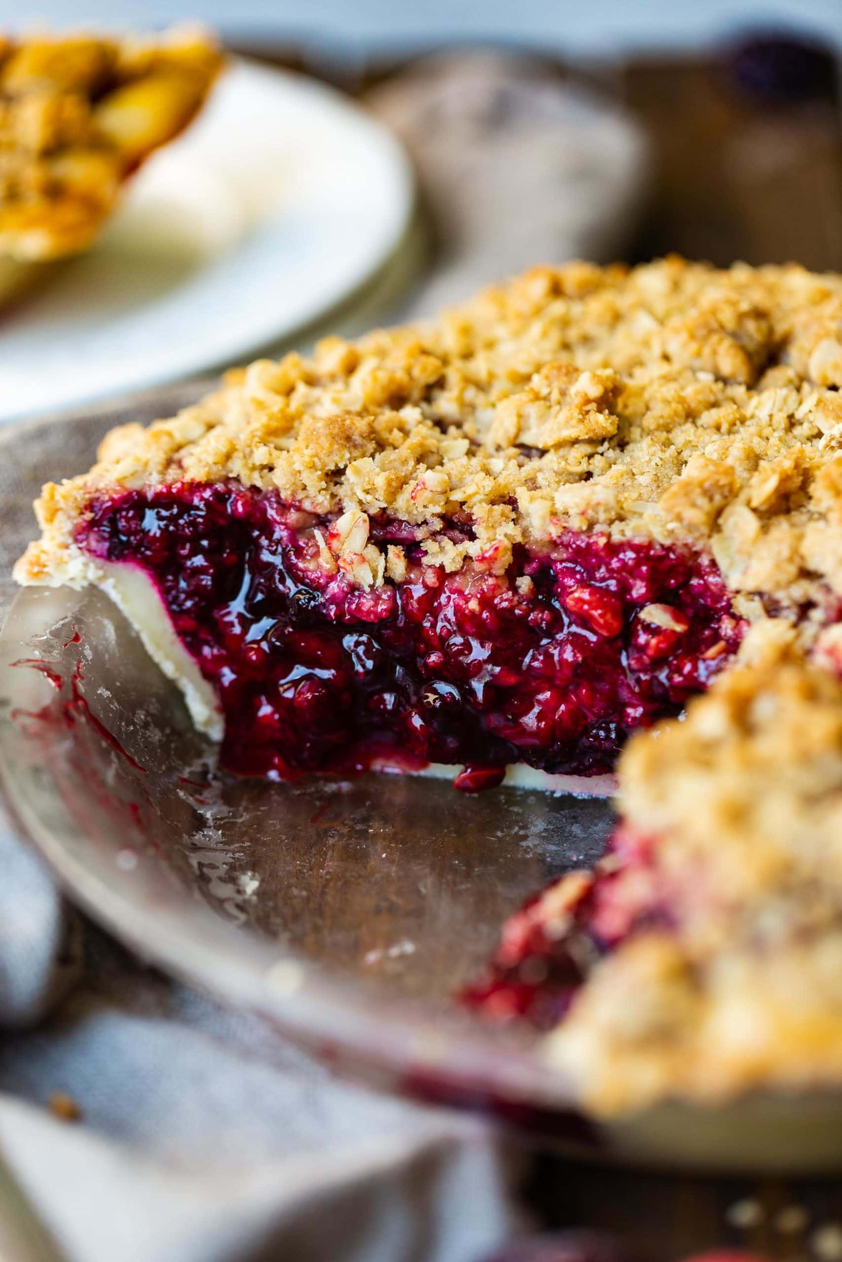 a photo of a whole mixed berry pie topped with golden streusel with a slice missing from the pie so you can see the cross-section of the pie.