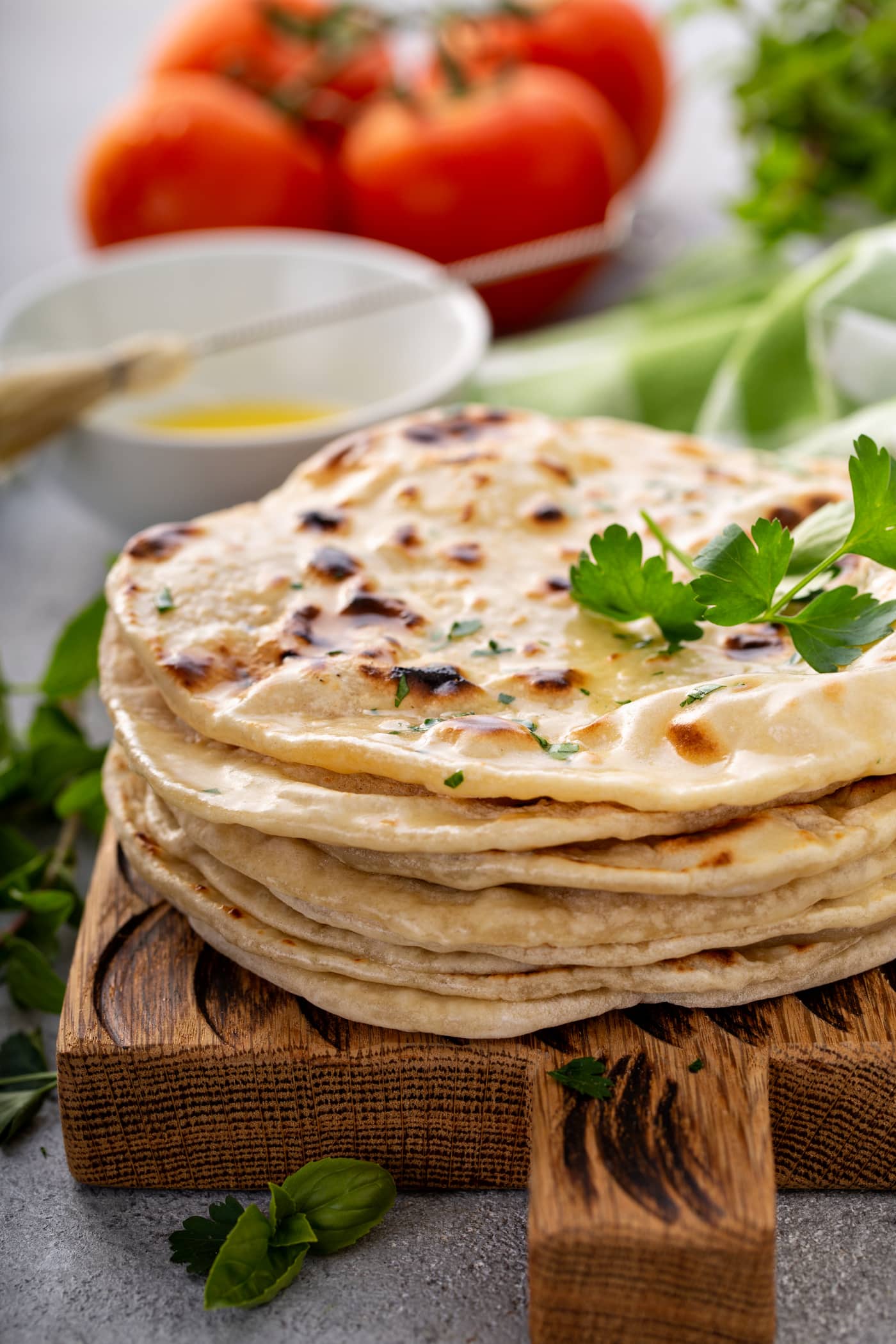 A photo of a stack of cooked discs of unleavened bread topped with chopped fresh parsley and a sprig of fresh parsley.