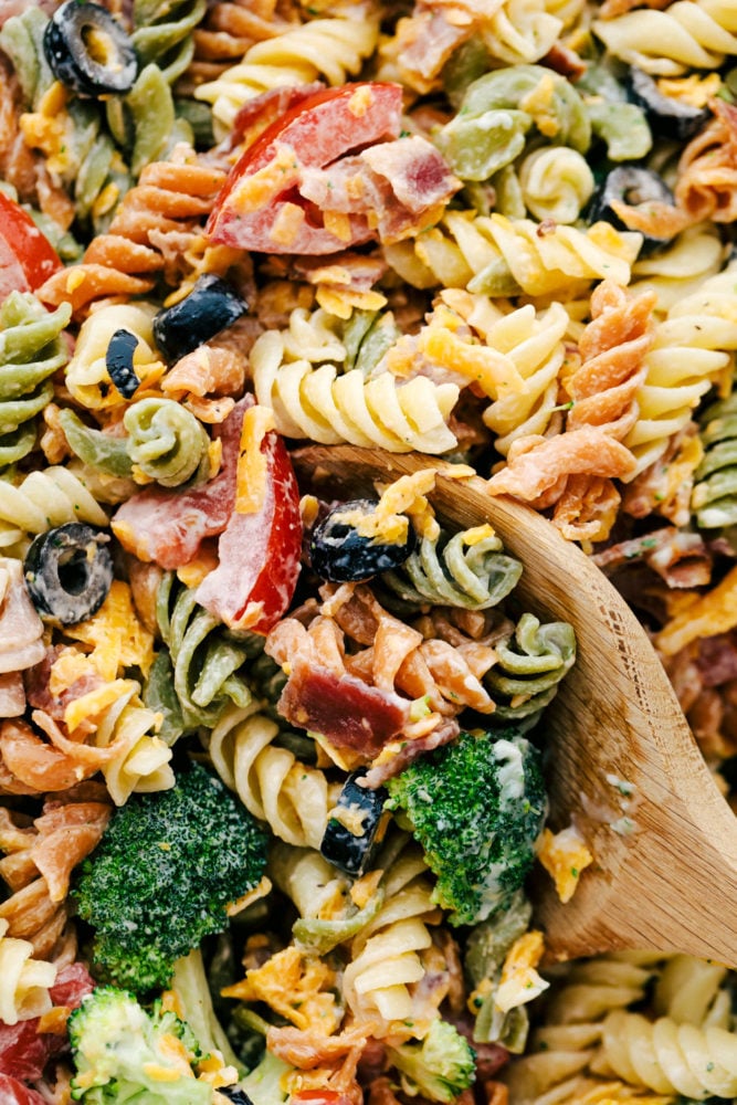 Close up on bacon ranch pasta salad ingredients being scooped up with a wooden spoon.