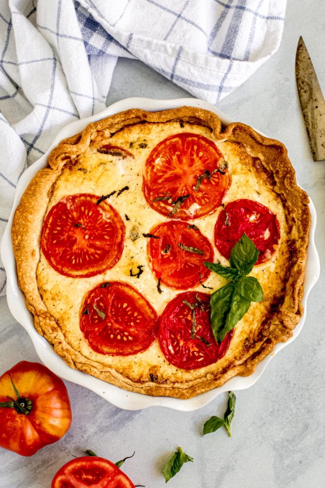 Tomato pie in a white pie dish with fresh basil on top