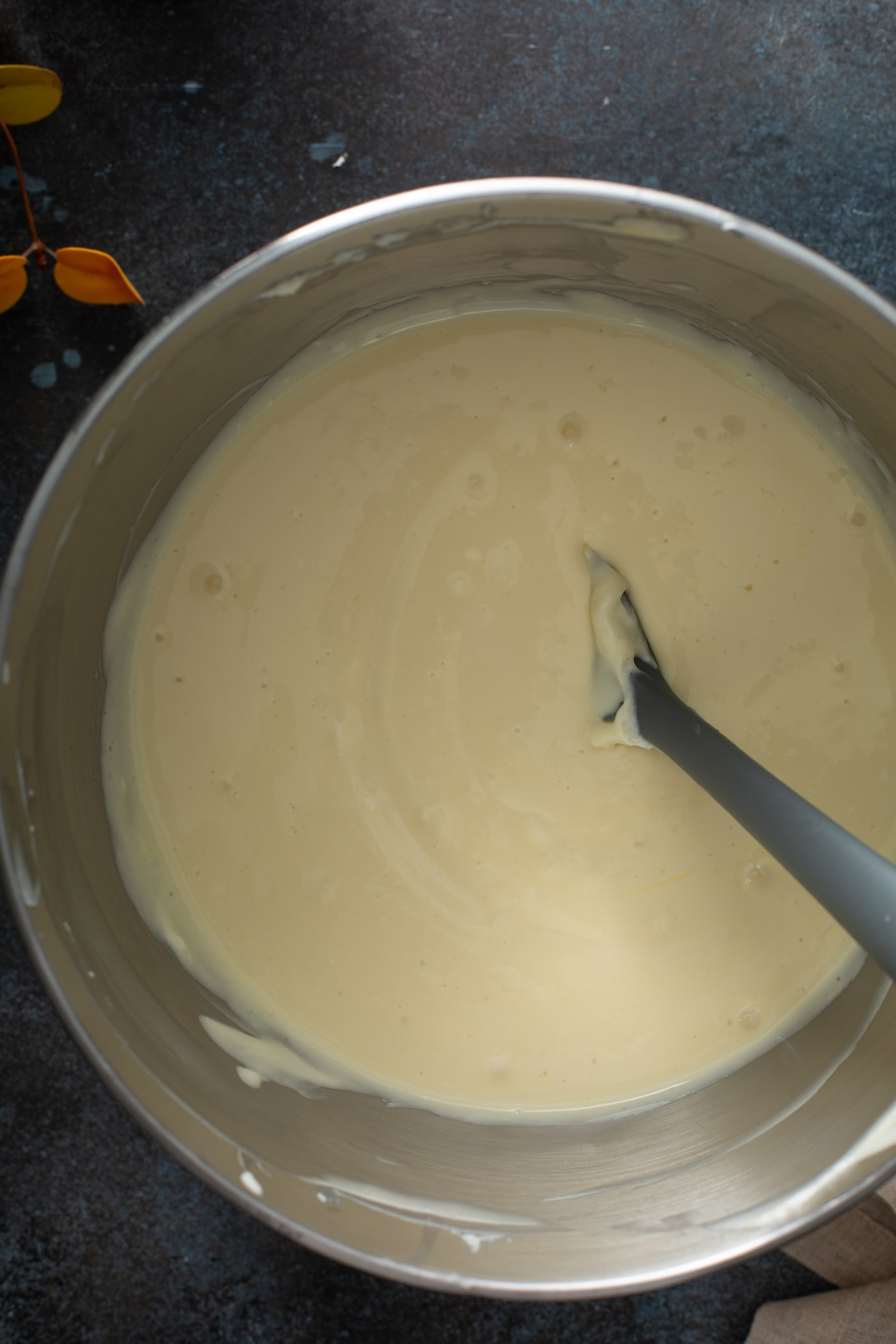 Cheesecake filling that has been mixed together in a bowl. a spoon is in the filling.