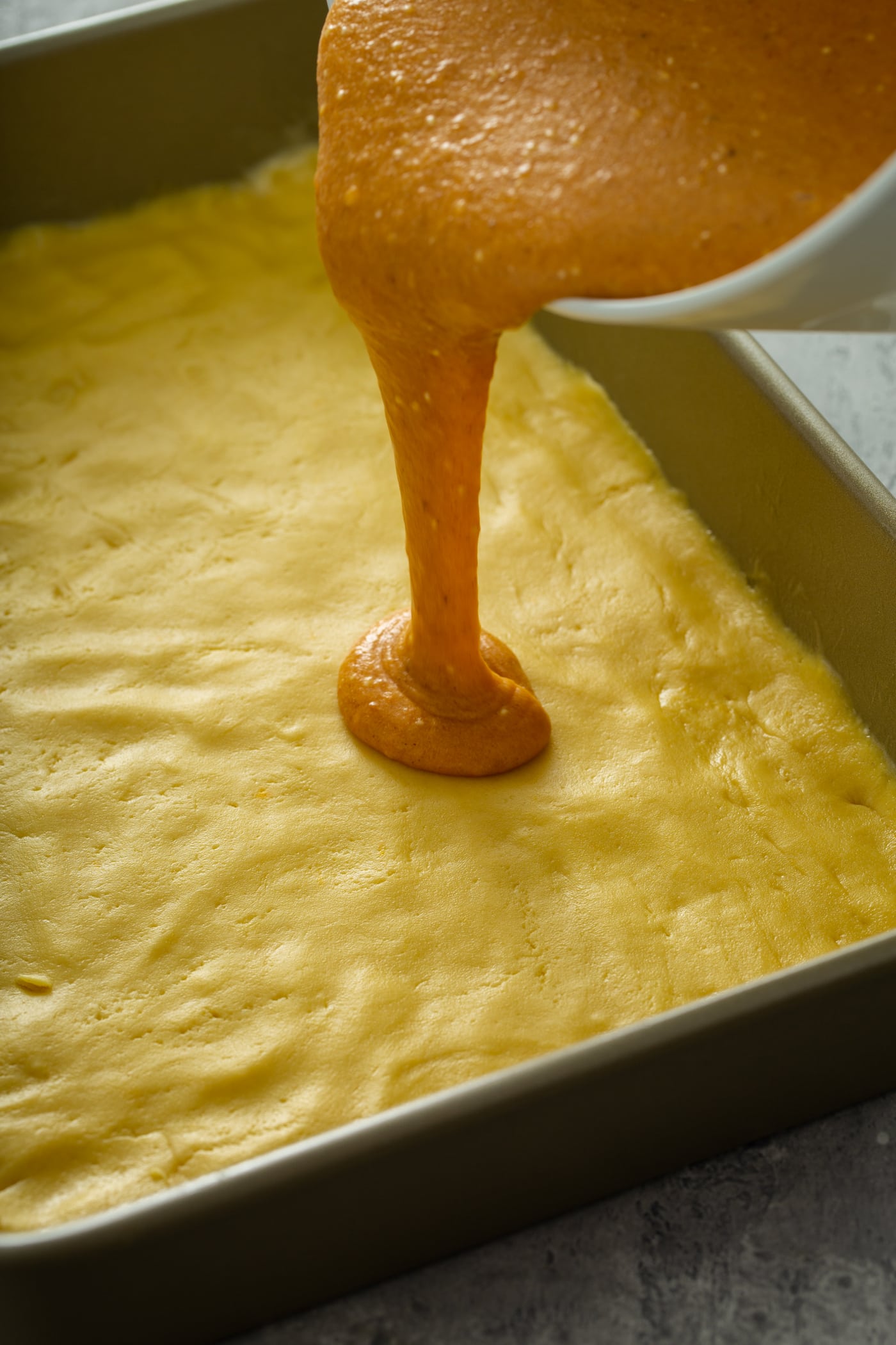 Pumpkin mixture being poured over yellow cake mix crust.