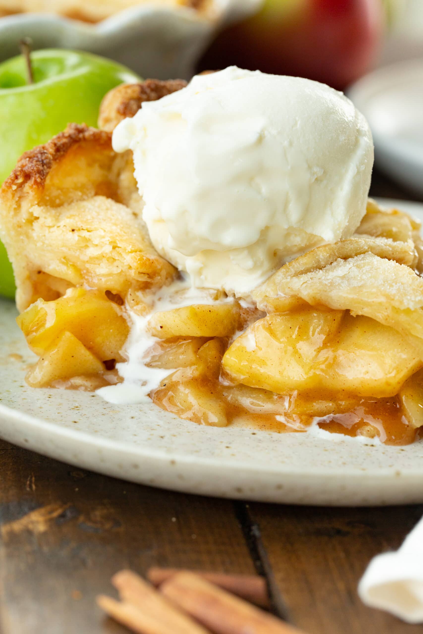 a photo of a slice of homemade apple pie with a golden lattice top and cooked cinnamon apples inside topped with a scoop of vanilla ice cream.