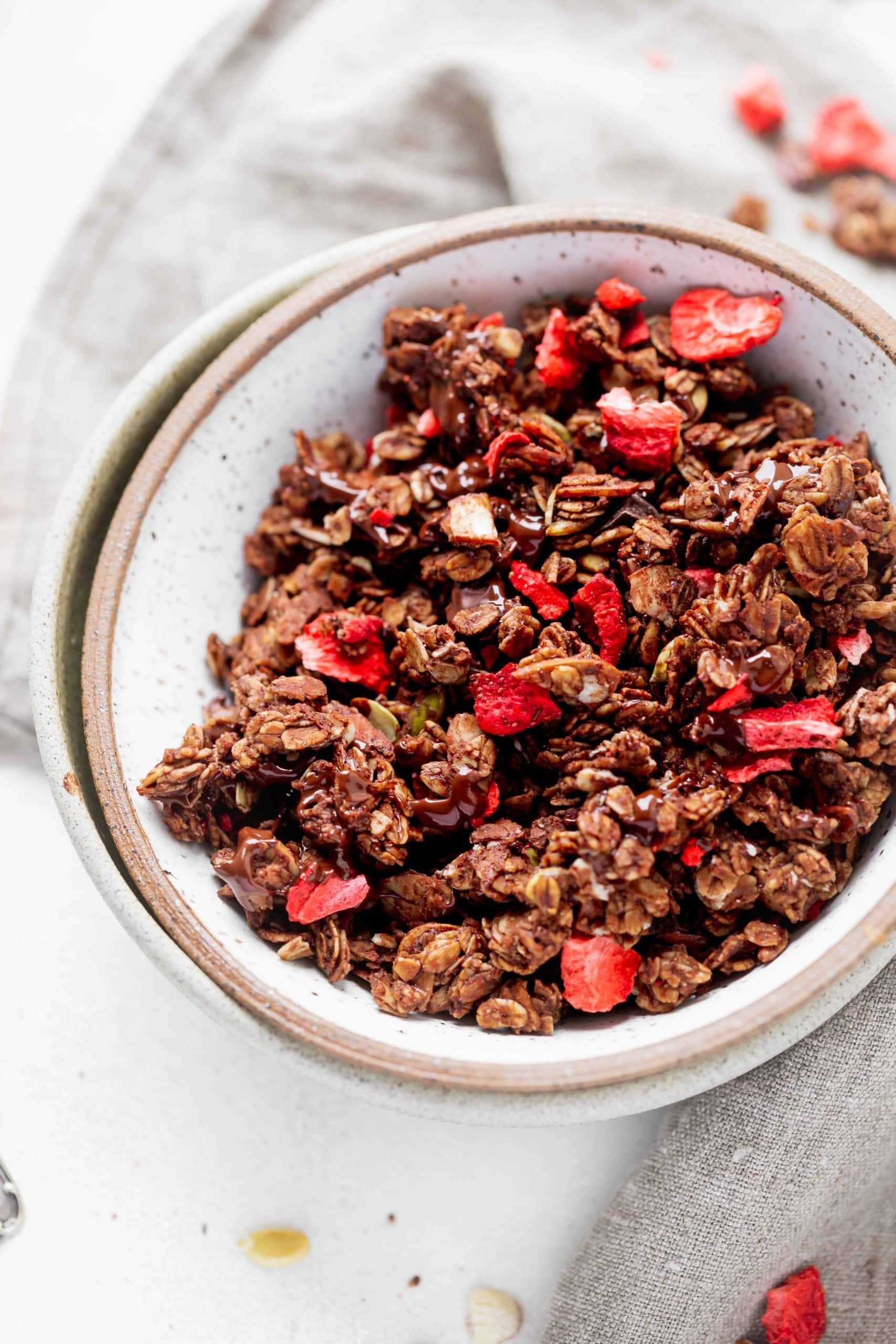 A bowl of chocolate lovers granola with strawberries. You can see the chunks of oats coated in chocolate and the red strawberries.
