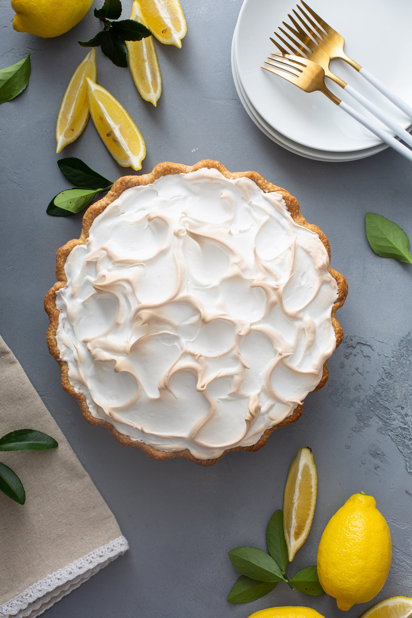 A picture of a lemon meringue pie. the meringue is fluffy and slightly browned. There are lemon wedges next to the pie.