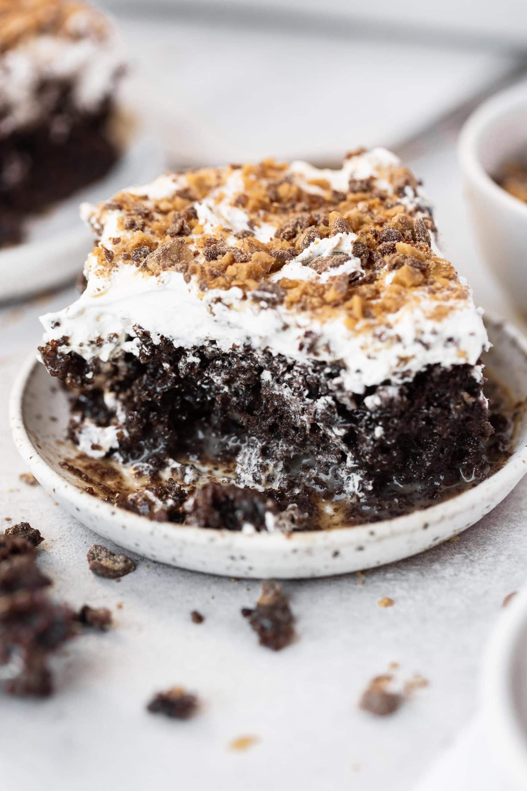 a photo of a piece of better than anything cake sitting on a small saucer with a bite missing from the corner of the cake.