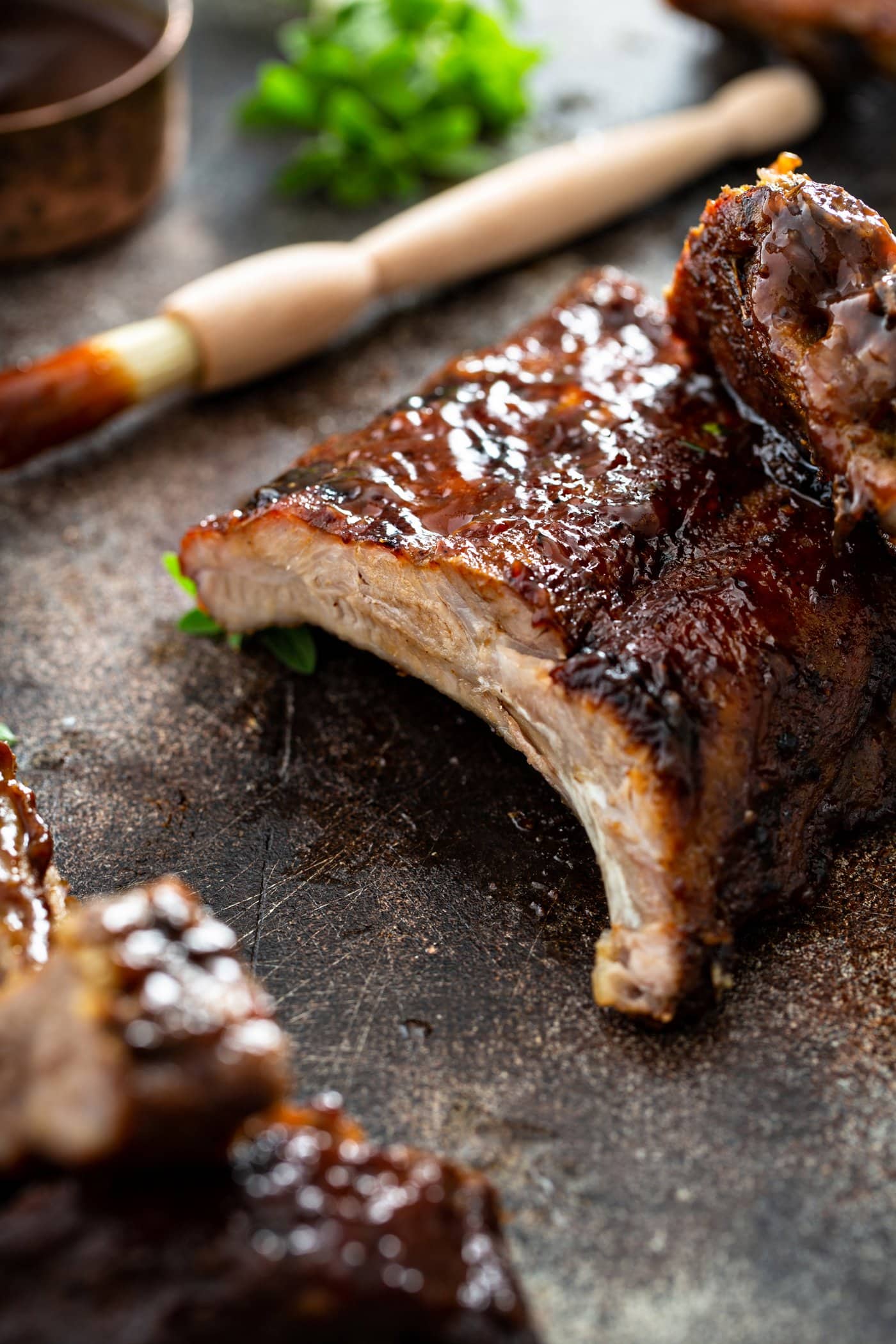 A rack of ribs that have been grilled. A couple of ribs have been cut from the rack. A brush with bbq glaze is next to the rack of ribs.