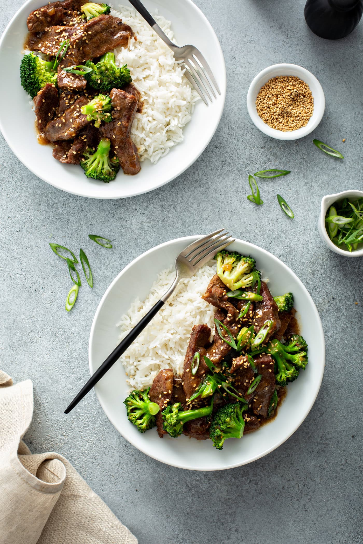 A photo of two bowls of beef and broccoli with a side of white rice.