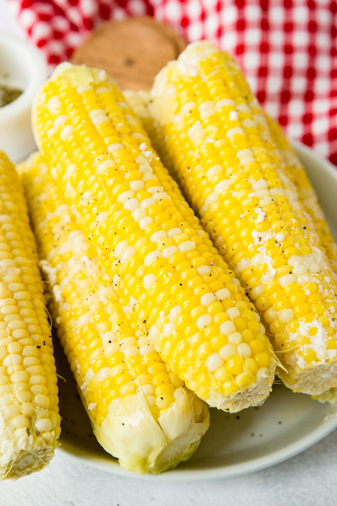 Four ears of cooked corn on the cob. The plate of corn is sitting on a red checked tea towel.