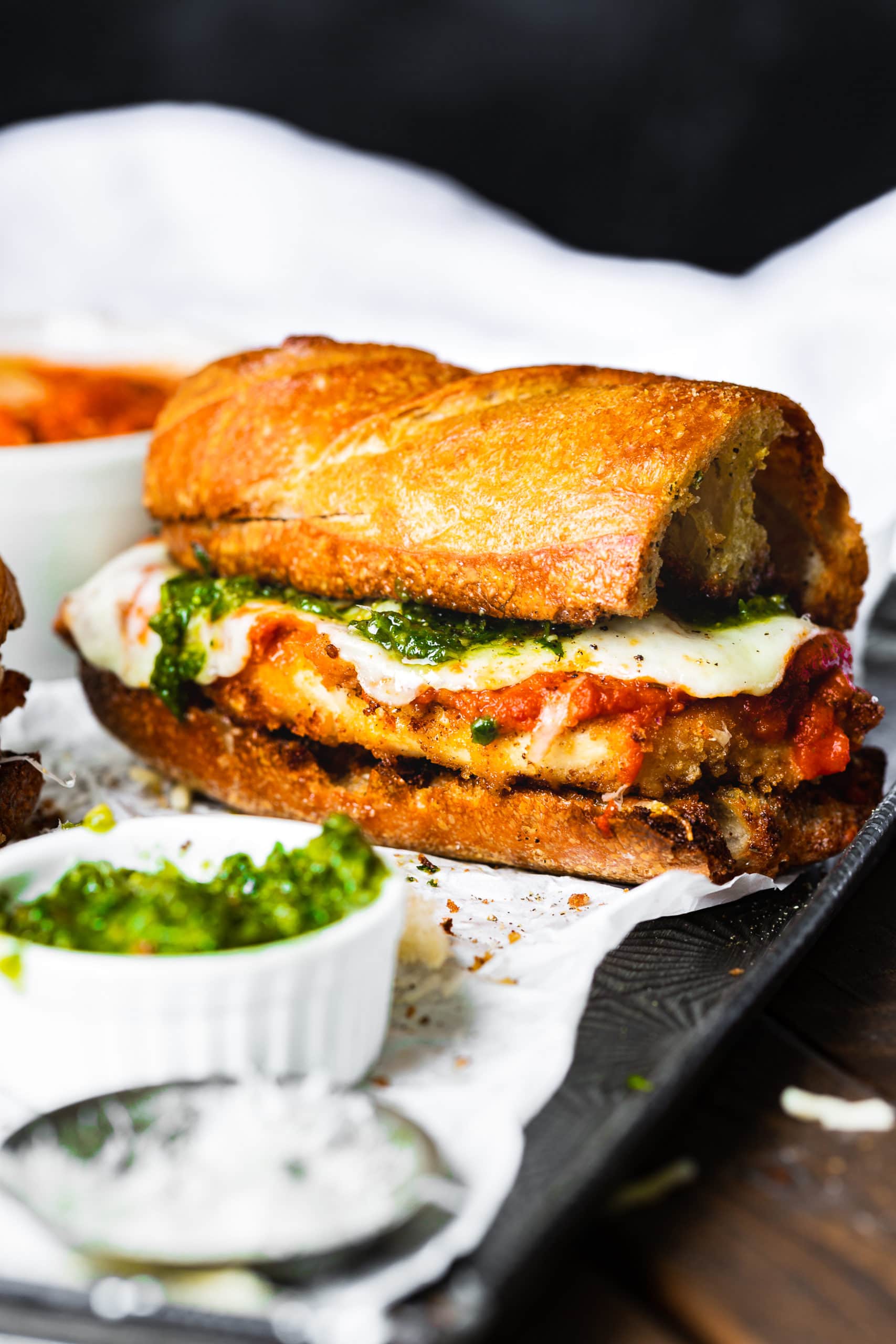 a photo of a chicken parm sandwich made on garlic bread with juicy chicken, melted mozzarella cheese and pesto.