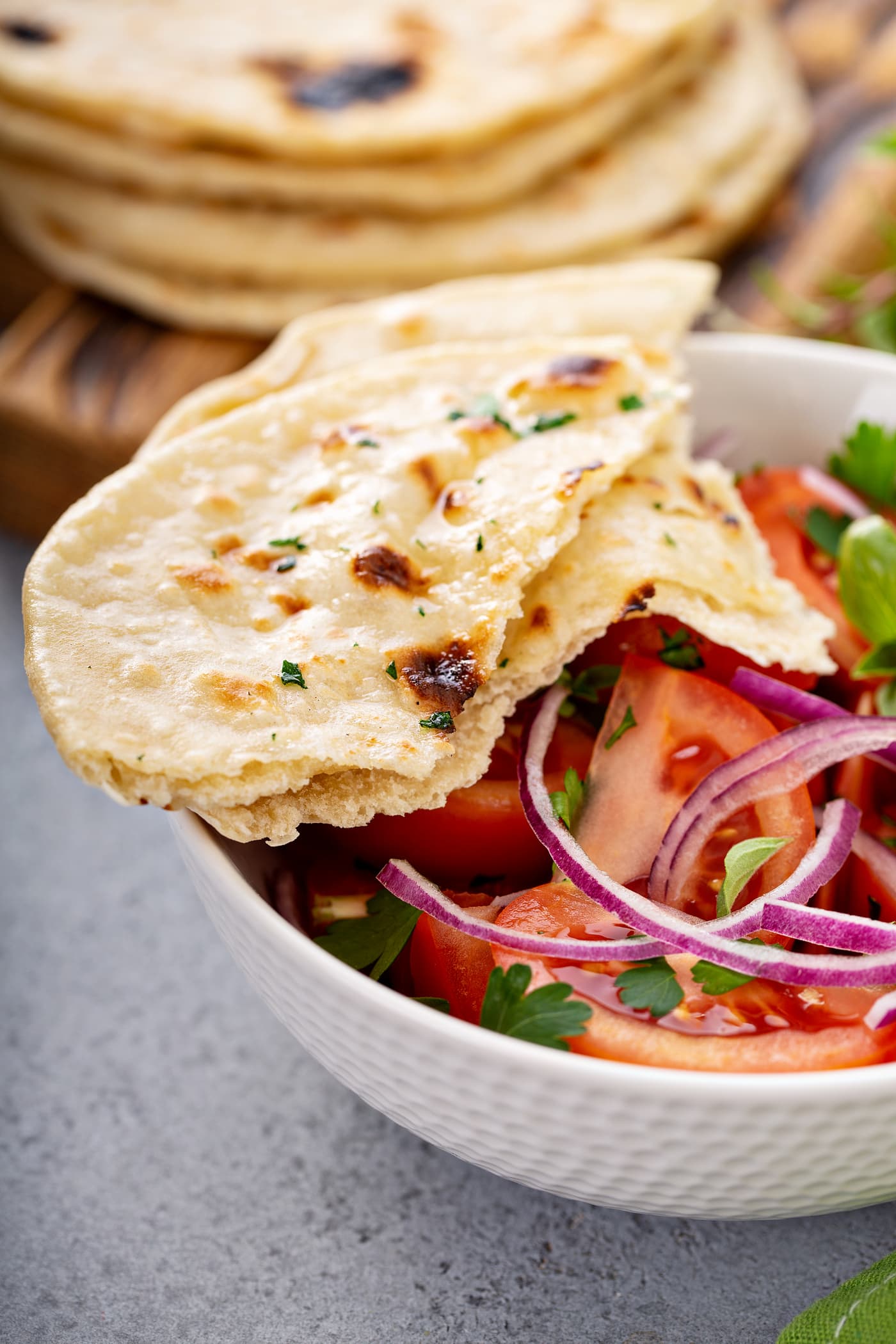 A photo of a bowl of fresh tomato and onion salad in a white bowl with torn pieces of unleavened bread sitting on the side of the bowl.