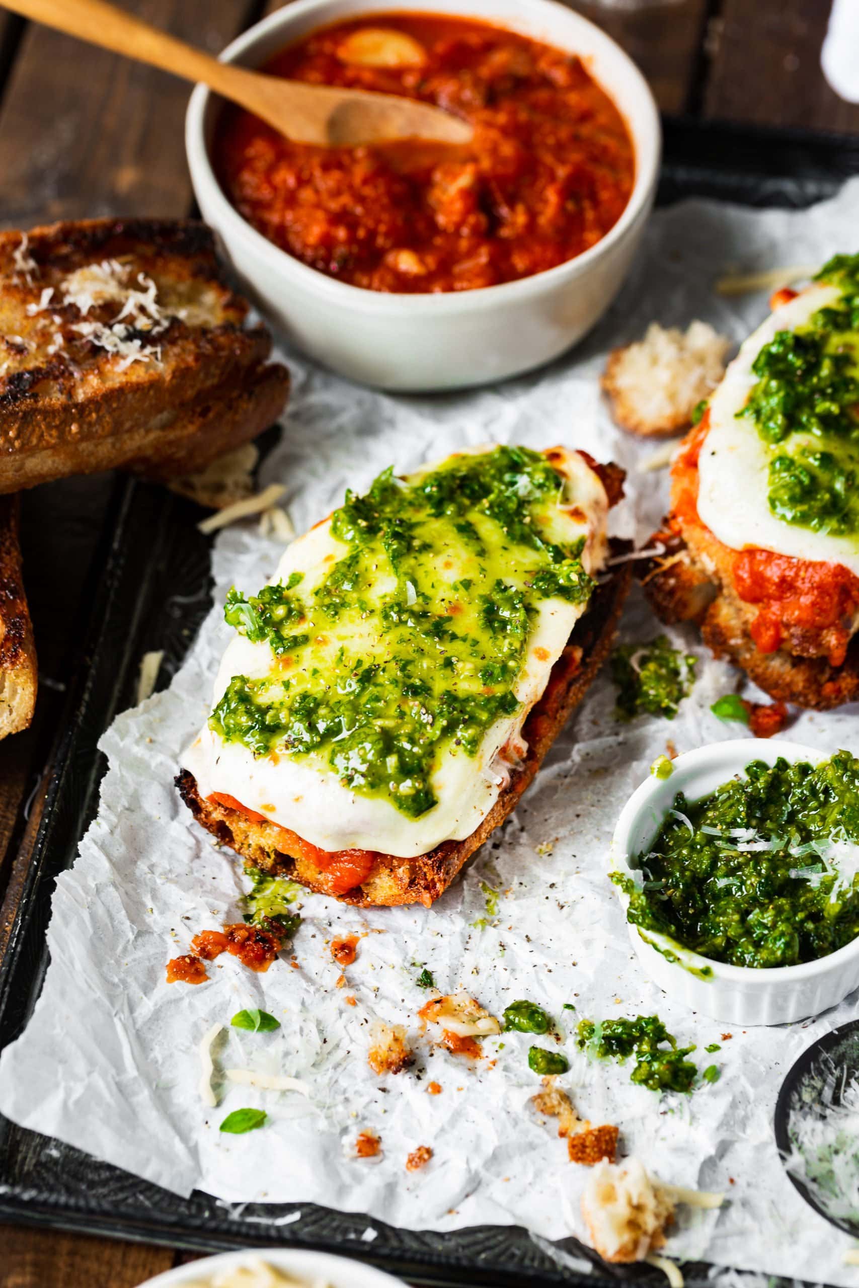 a photo of the bottom half of two parmesan chicken sandwiches with the tops off showing the melted mozzarella on top of the breaded chicken breasts with pesto on top.