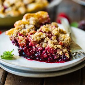 a photo of a piece of dutch berry pie sitting on a small white dessert plate with an oat streusel on top and golden crust on the bottom.