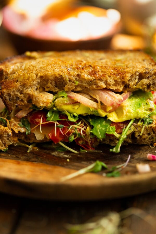 a photo of an avocado sandwich with toasted multigrain bread, bean sprouts, red onions, avocado, arugula, etc.