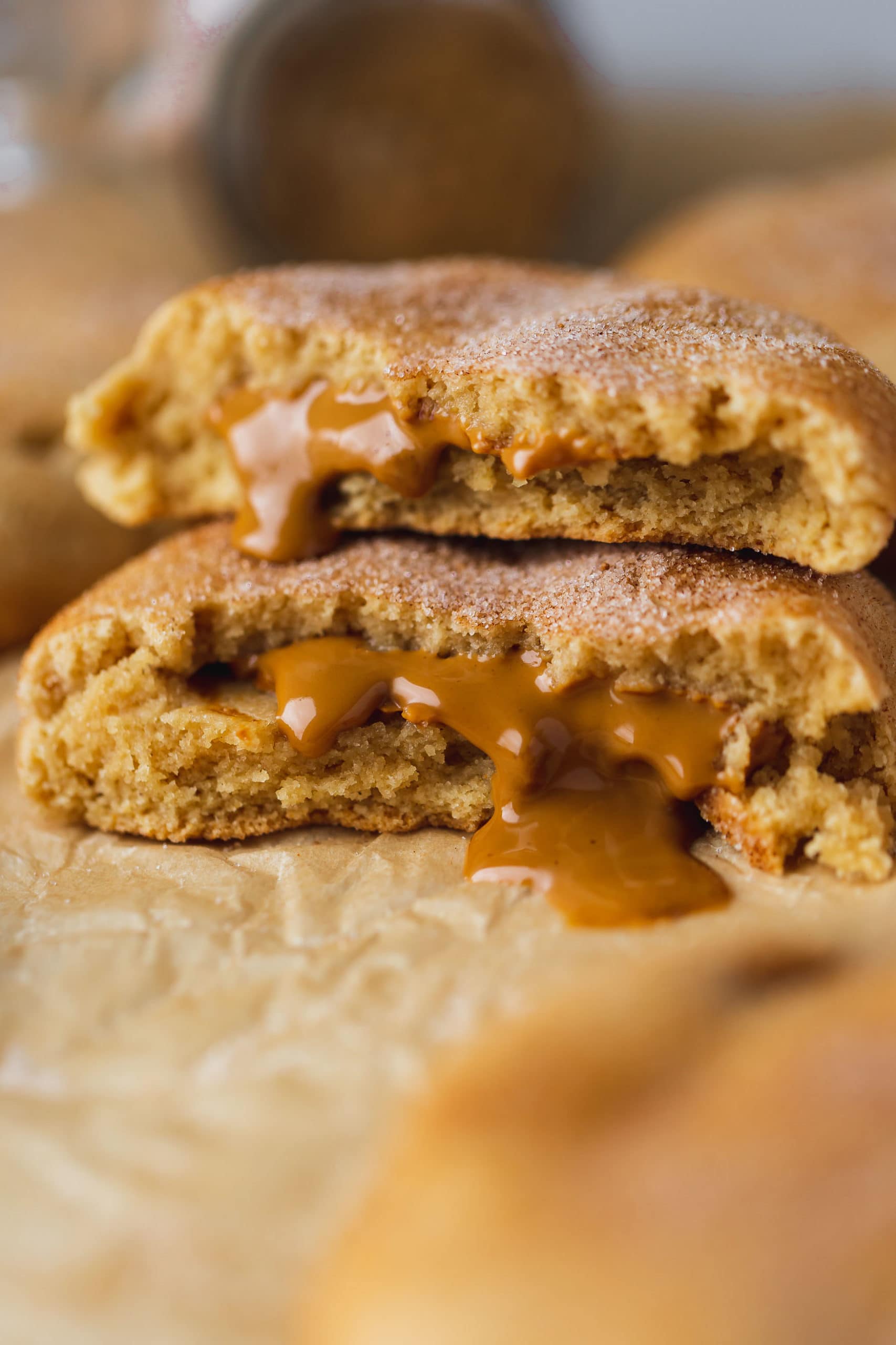 A biscoff stuffed snickerdoodle broken in half and the halves are stacked on top of each other. The biscoff center is oozing out onto the parchment paper.