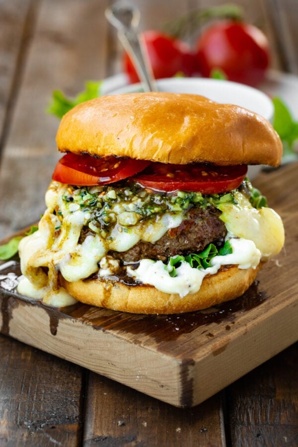 a photo of a garlic pesto burger topped with melted havarti cheese, pesto, bright red tomatoes all on a brioche bun. a photo of a garlic pesto burger topped with melted havarti cheese, pesto, bright red tomatoes all on a brioche bun.