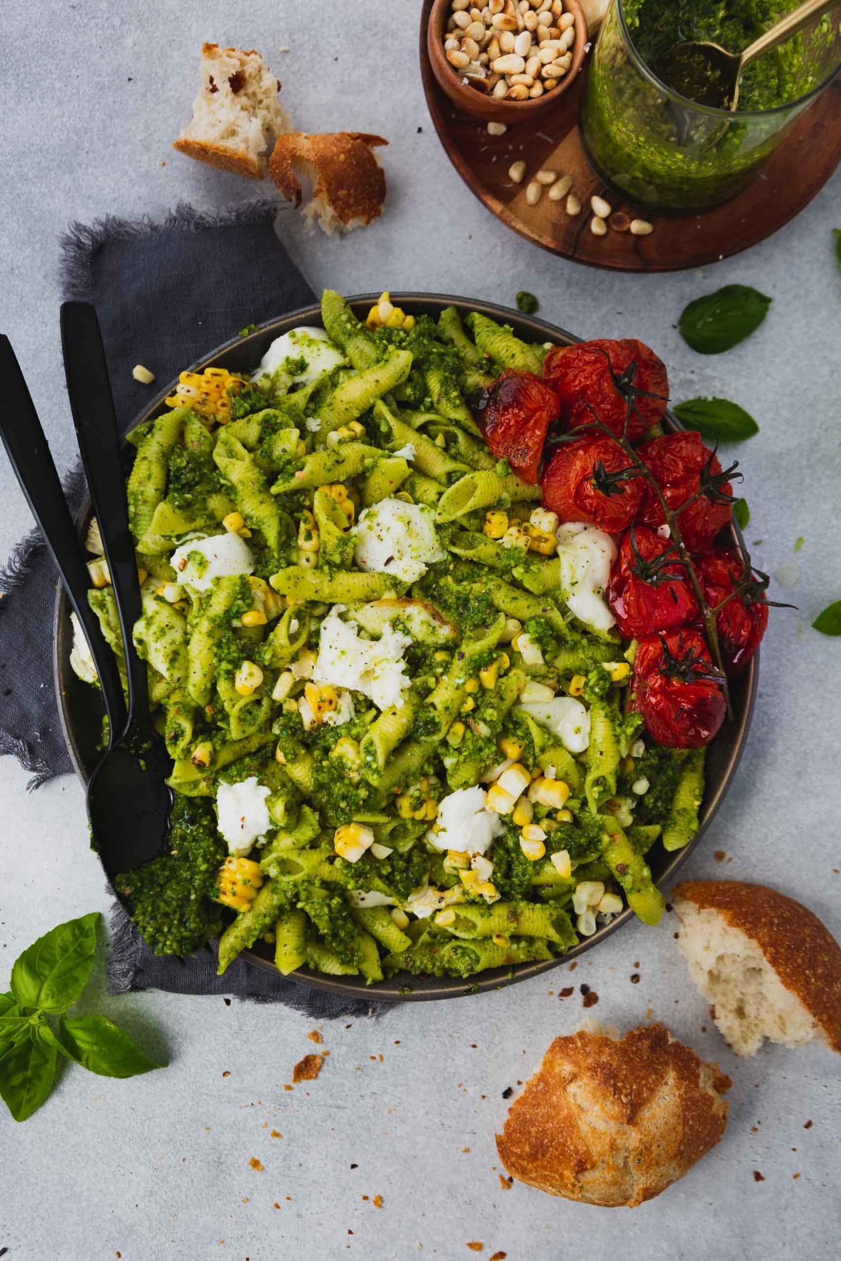 a photo of a large bowl full of pasta covered in homemade pesto and topped with roasted tomatoes, grilled corn and mozzarella balls.