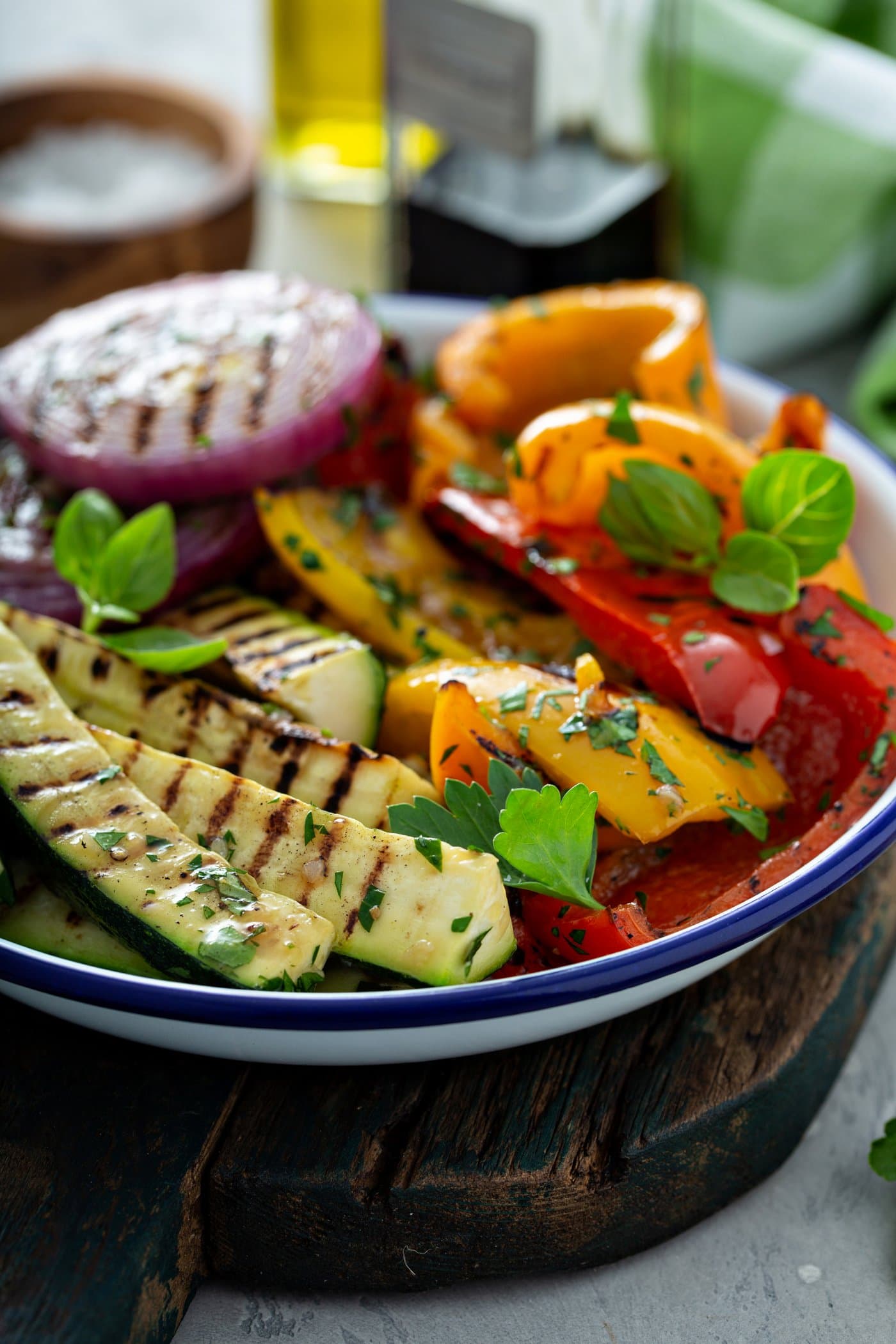 A serving dish of grilled zucchini, red and yellow bell peppers and red onions. There are golden grill marks on the vegetables and parsley leaves sprinkled on top.