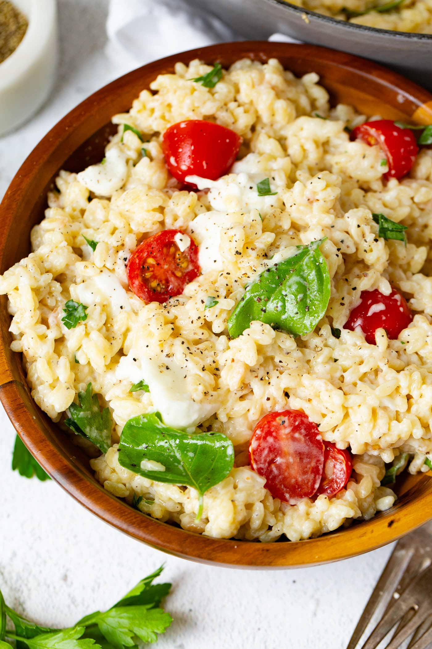 A bowl of caprese orzo salad with fresh tomatoes, mozzarella chunks and fresh basil. A few basil leaves are on the table next to the pasta.