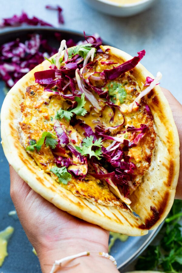 a piece of golden pita bread lined with a golden cooked ground chicken patty that is lathered in curry sauce and topped with radicchio and cilantro.